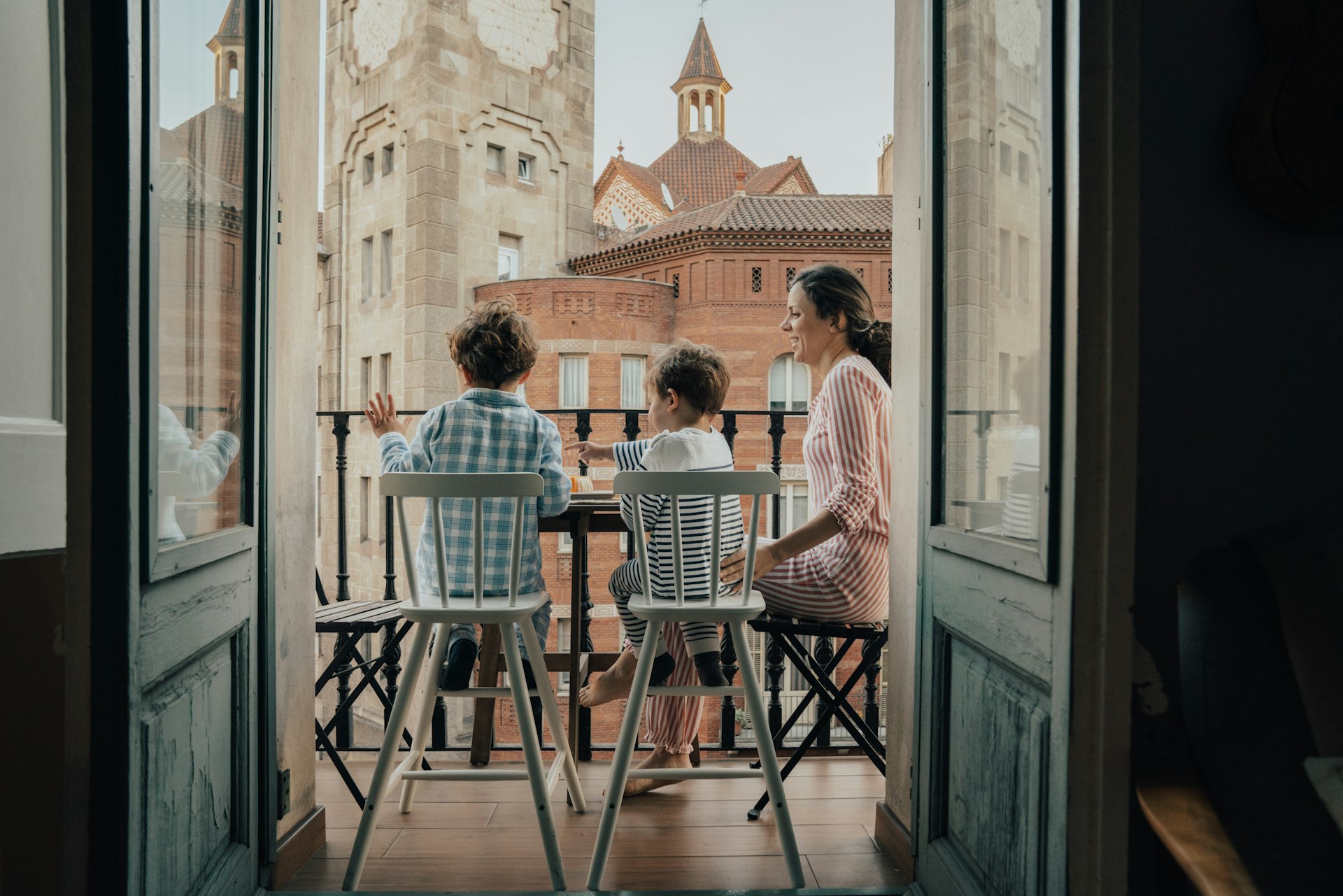 Two small children and their mother sit on a balcony overlooking historic architecture in Barcelona