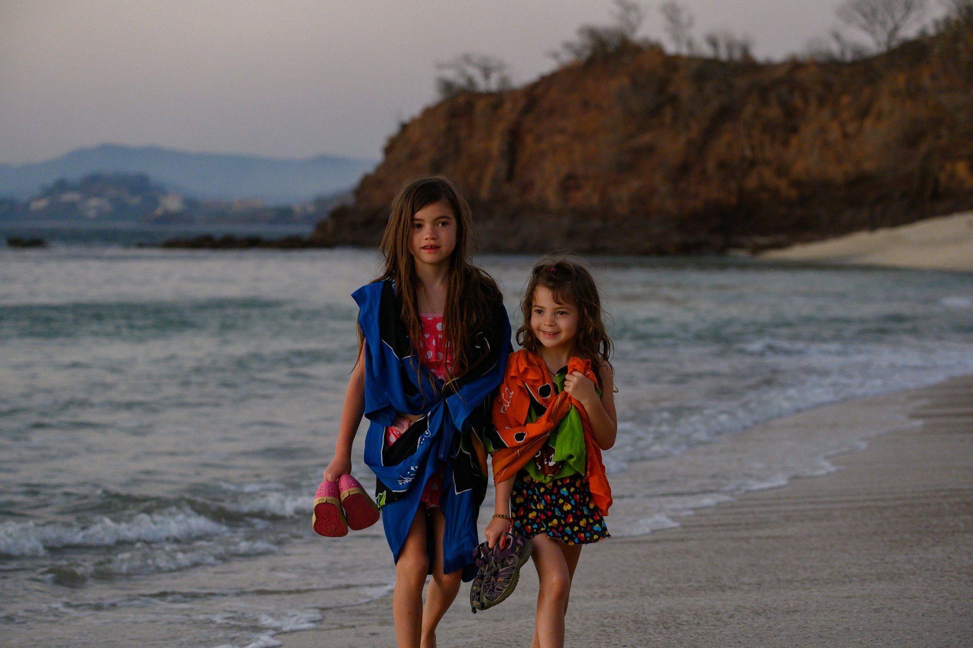 Two young girls walking alongside each other on a beach in Central America
