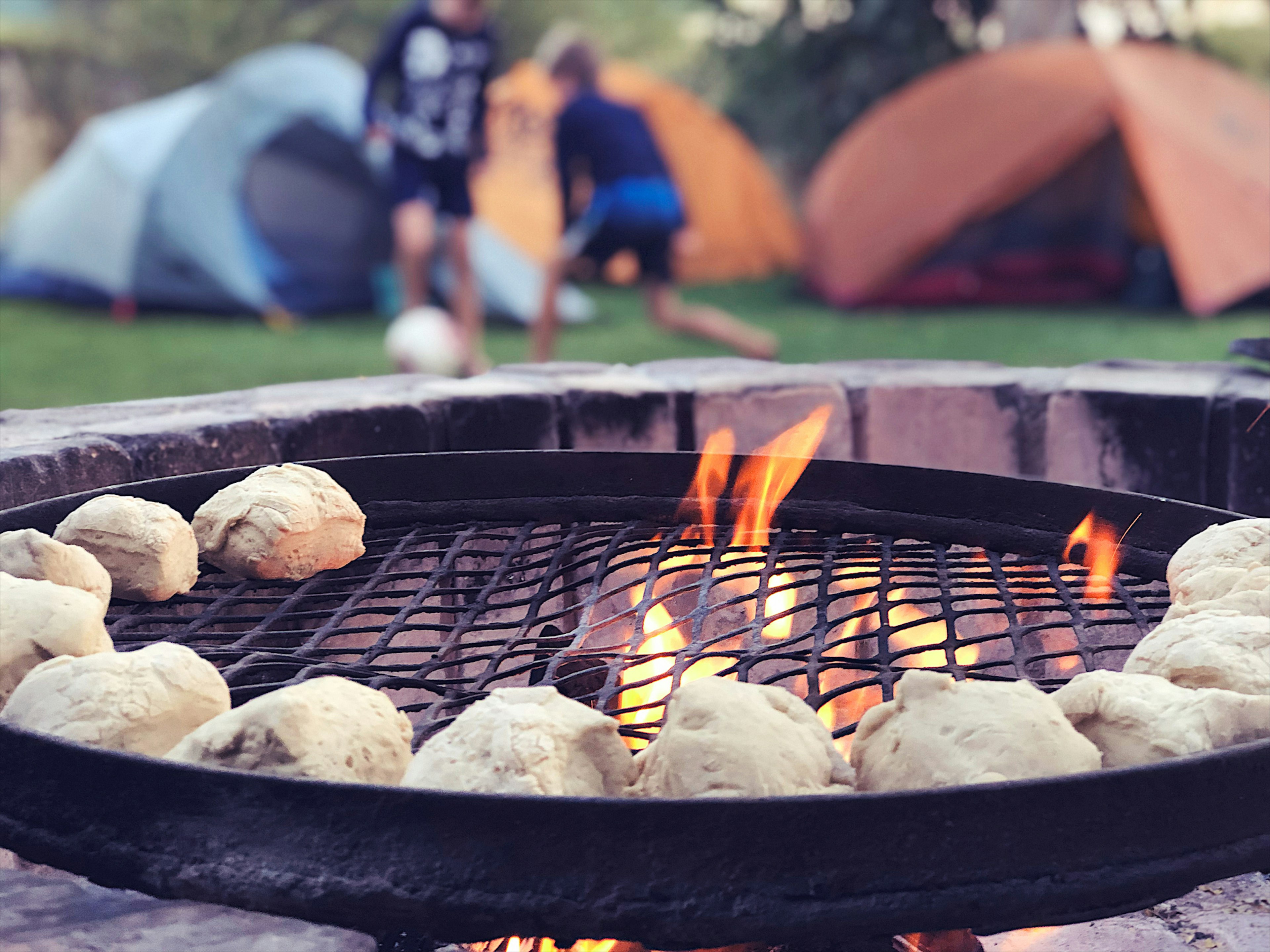 Two kids play football between tents at a campsite and a barbecue