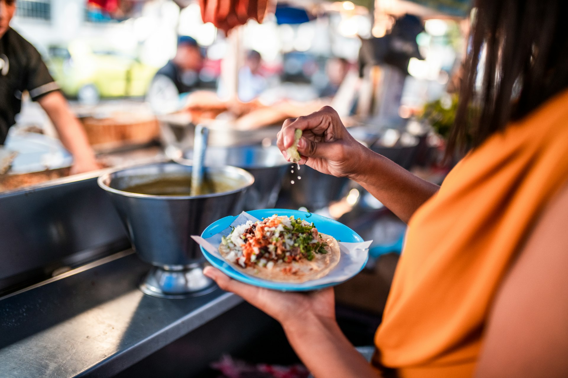 A woman squeezes a lime on a taco in front of a Mexican street food stand