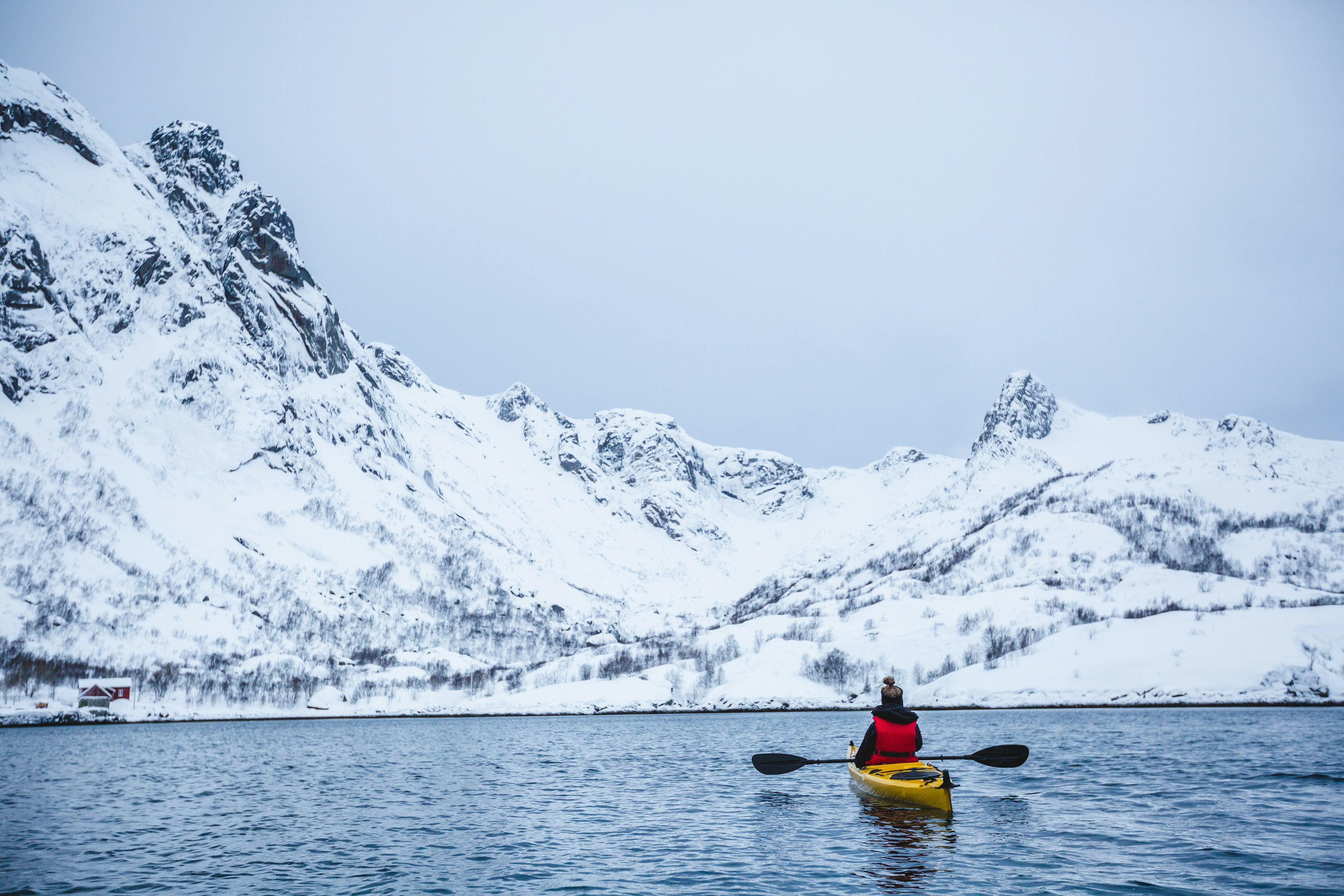 Rear view of woman kayaking in a lake near a snowy mountainous landscape