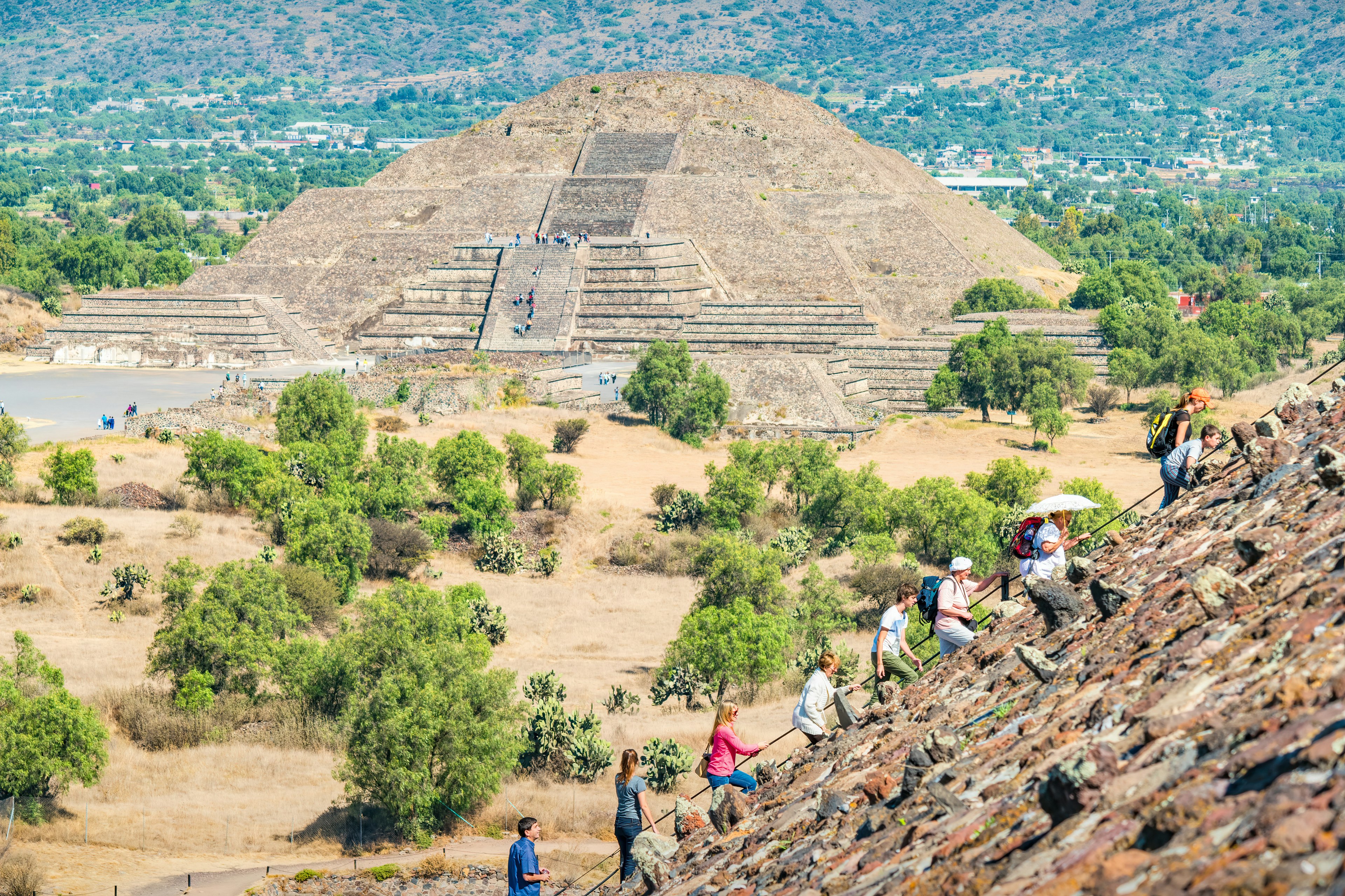 Tourists climb the Pyramid of the Sun at the Teotihuacan pyramids, near Mexico City, Mexico on a sunny day, with the Pyramid of the Moon in the background.