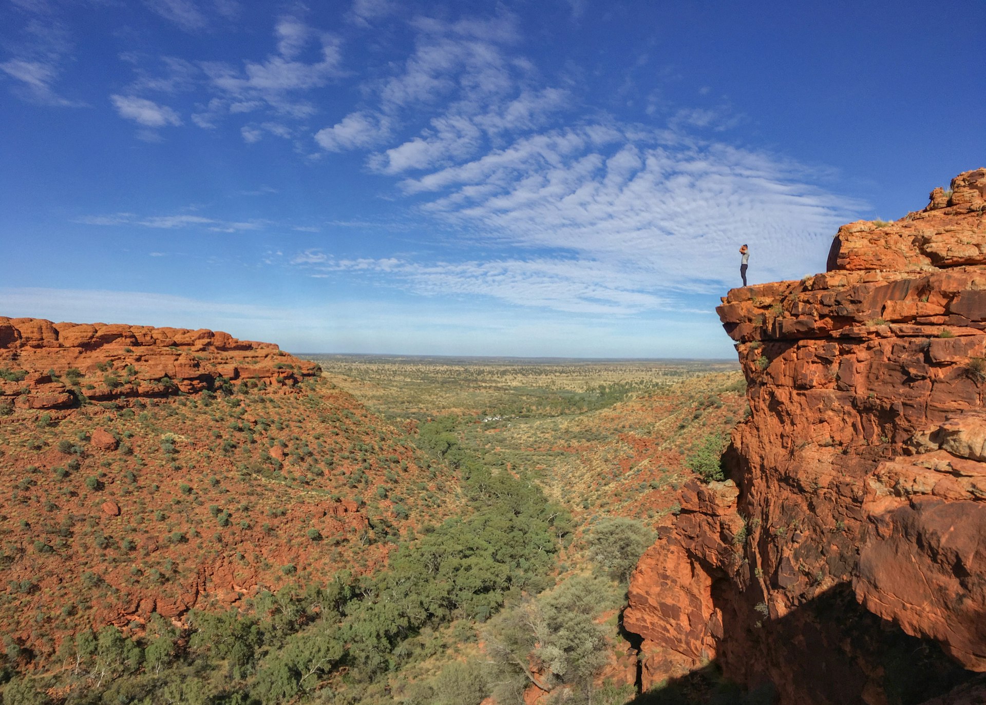 A solo figure stands on the edge of a red-rock cliff above a valley