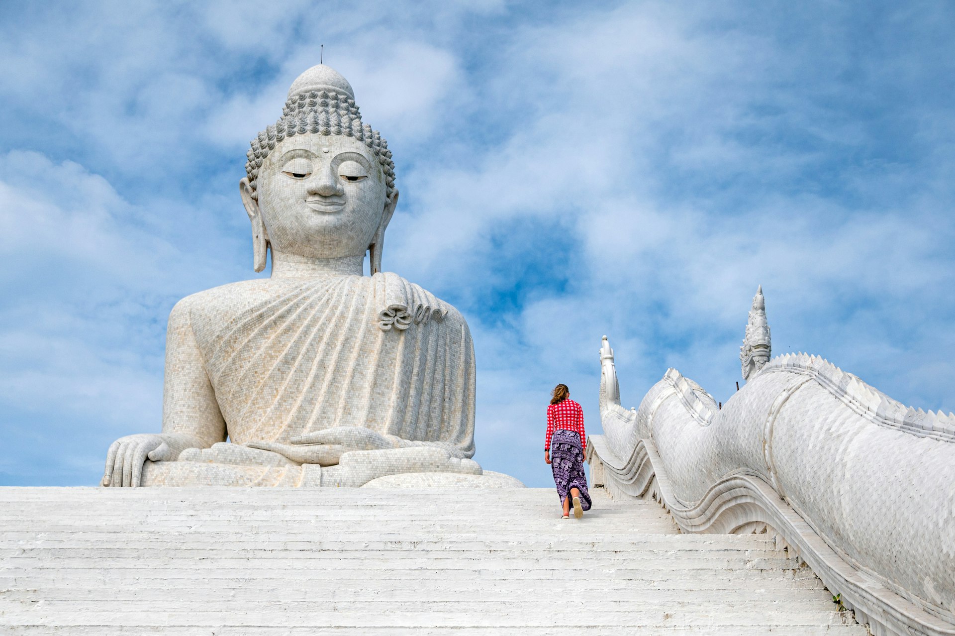 A teenager climbs steps upwards towards a vast white marble Buddha statue