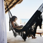 1366306539
Wide shot of a woman working on laptop while relaxing in a hammock in an ocean-view villa in Mexico