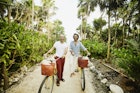 Two men laughing as they walk along a beach path with bikes in Mexico