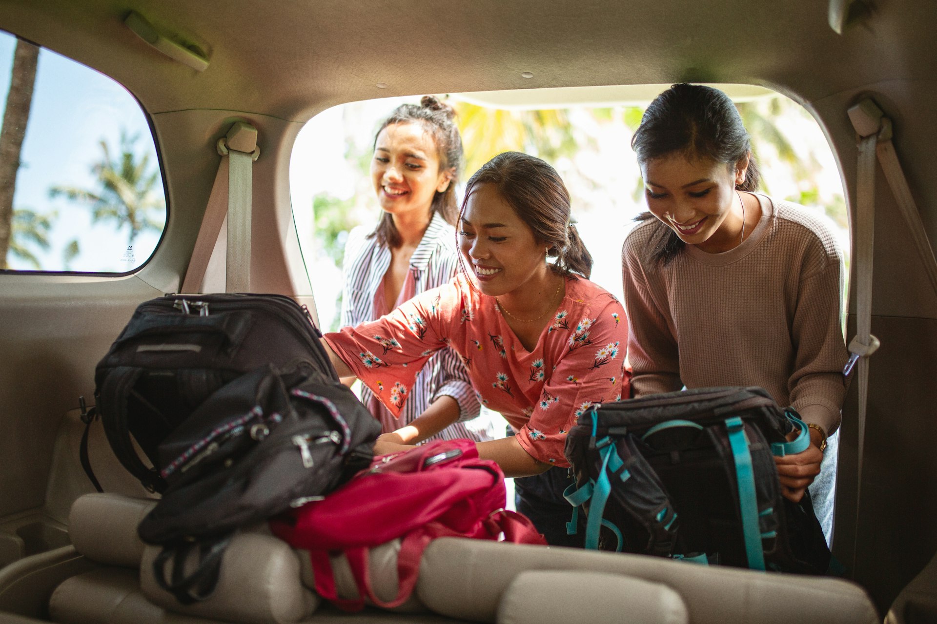 Three women put backpacks in the trunk of a car