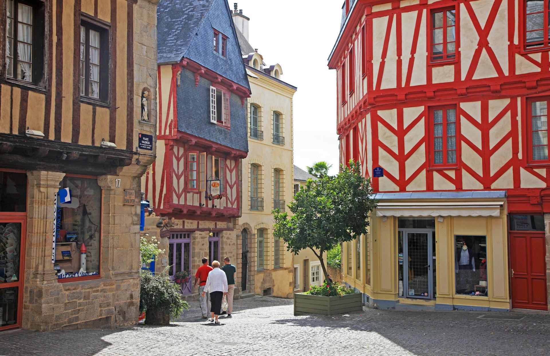 Tourists mill about the mediveal town center of Vannes with pretty wooden-timber houses and bright sunshine