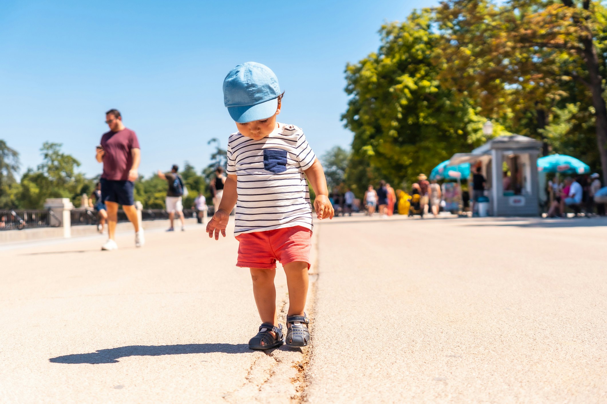 A toddler concentrates as he walks along a line in the ground in a park