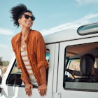 A beautiful black woman leaning out of the window of a jeep and smiling as it drives down the road