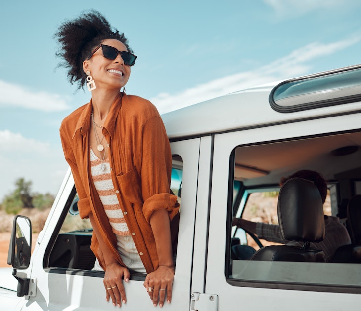 A beautiful black woman leaning out of the window of a jeep and smiling as it drives down the road
