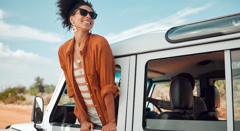 A beautiful black woman leaning out of the window of a jeep and smiling as it drives down the road