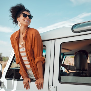 A beautiful black woman leaning out of the window of a jeep and smiling as it drives down the road