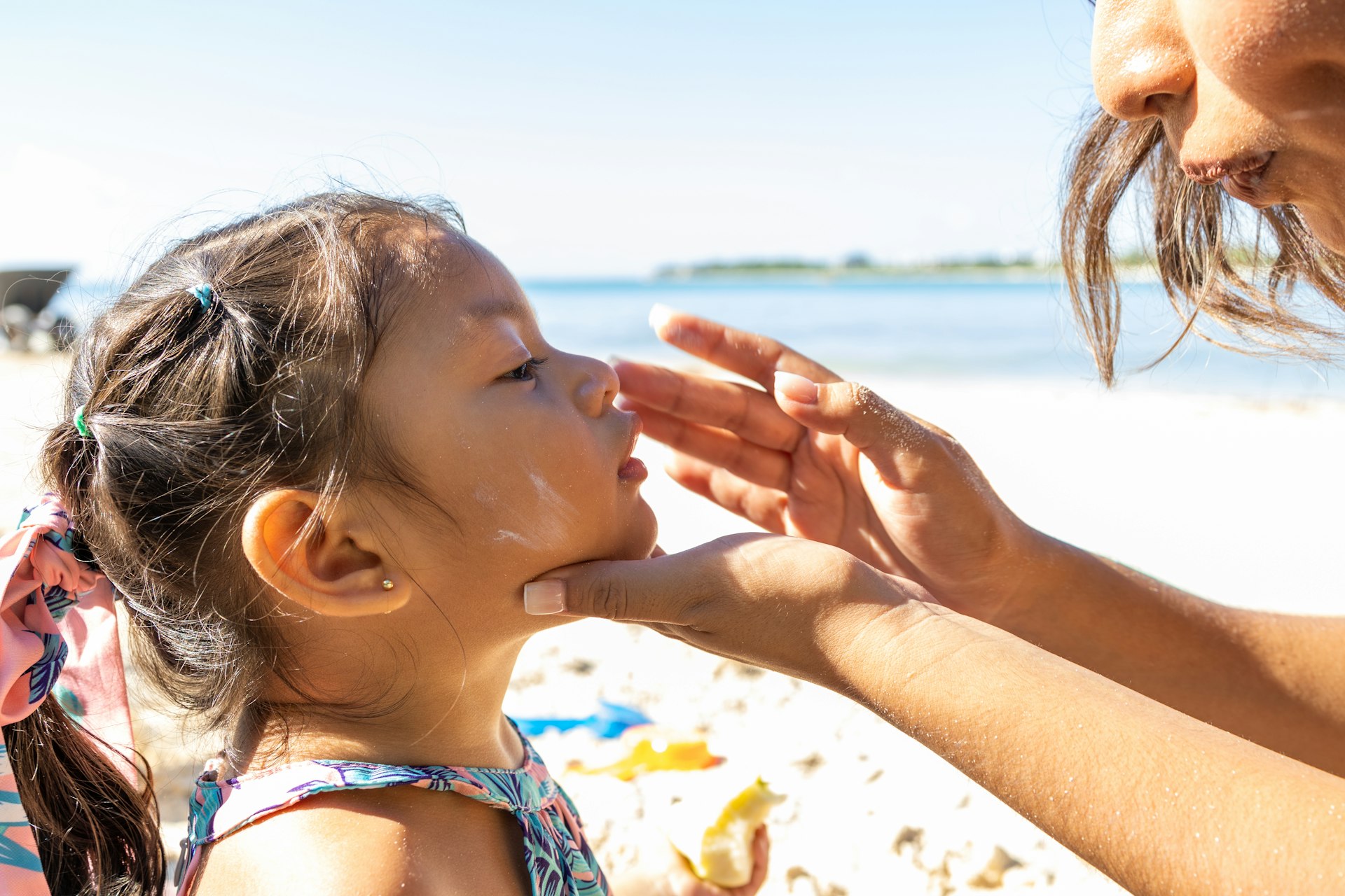 A mother puts sunscreen on her young daughter's face