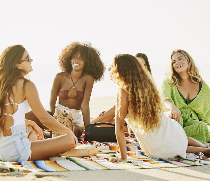 Smiling female friends relaxing on a blanket on a tropical beach at sunset while on vacation in Mexico