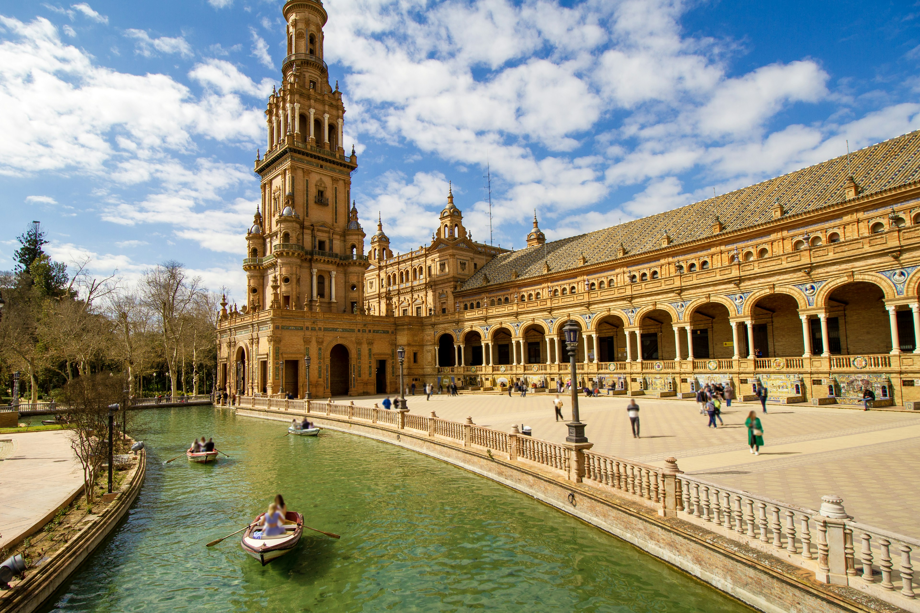 People paddle in canoes in the moat in front of a palace in Seville, Spain