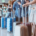 Travelers with luggage using smart phones while waiting in line for boarding at airport. Focus on wheeled luggage.
1473910675