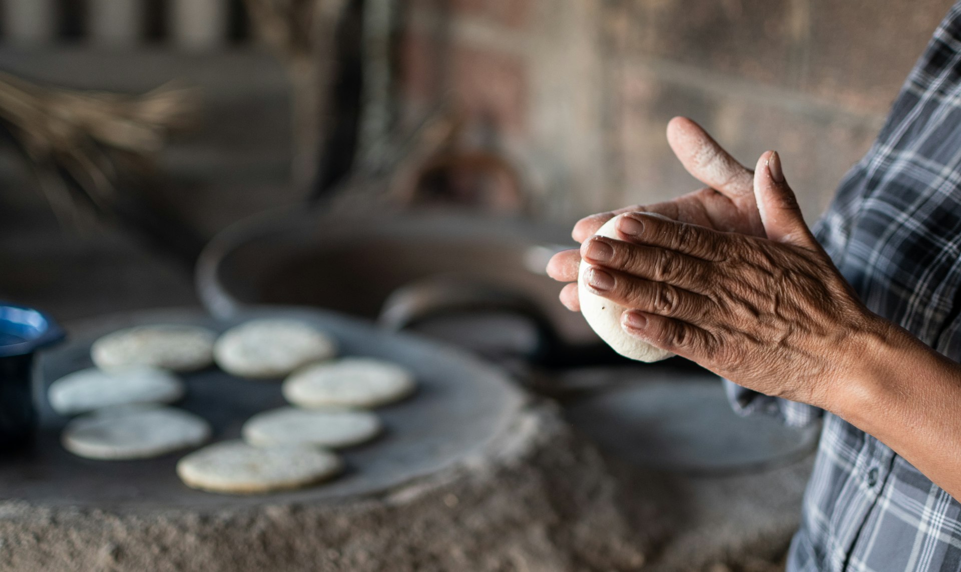 Closeup on a disc of dough between a woman's hands, making corn tortillas in a traditional way