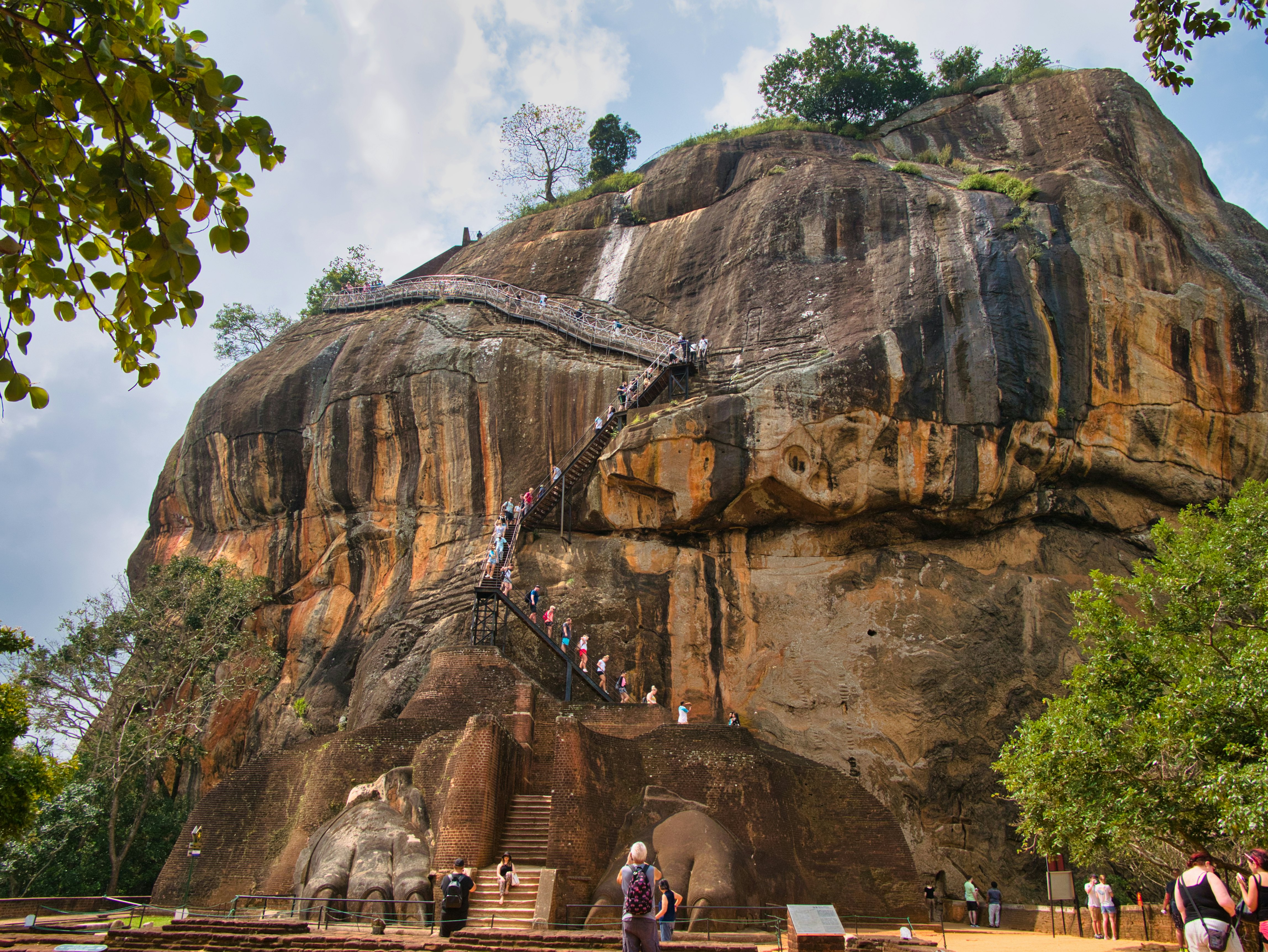 A wide shot of people climbing staircases along the sheer face of a rocky outcrop.