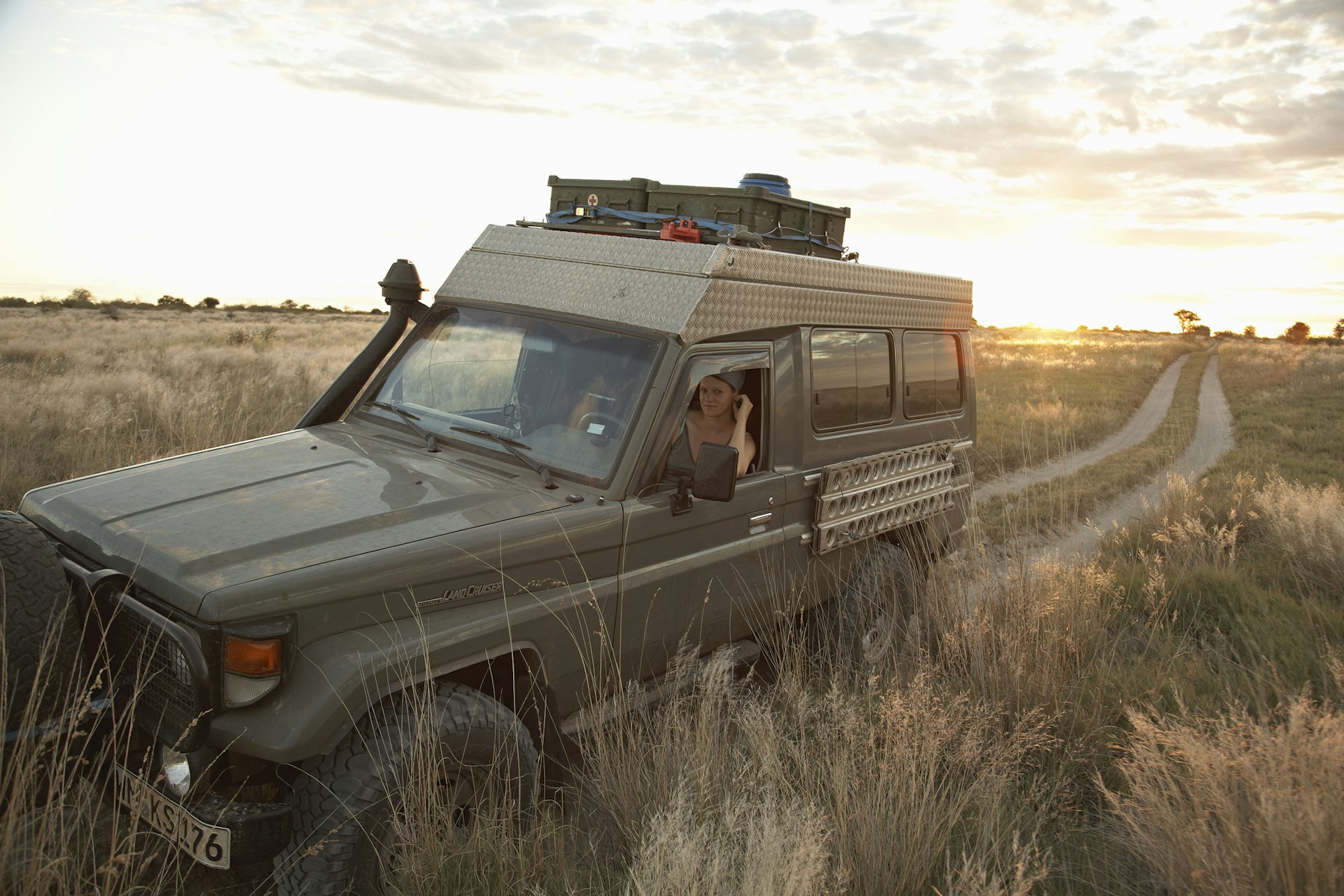A Land Cruiser cuts through the Bush in Botswana, following a dirt track with a women sat inside