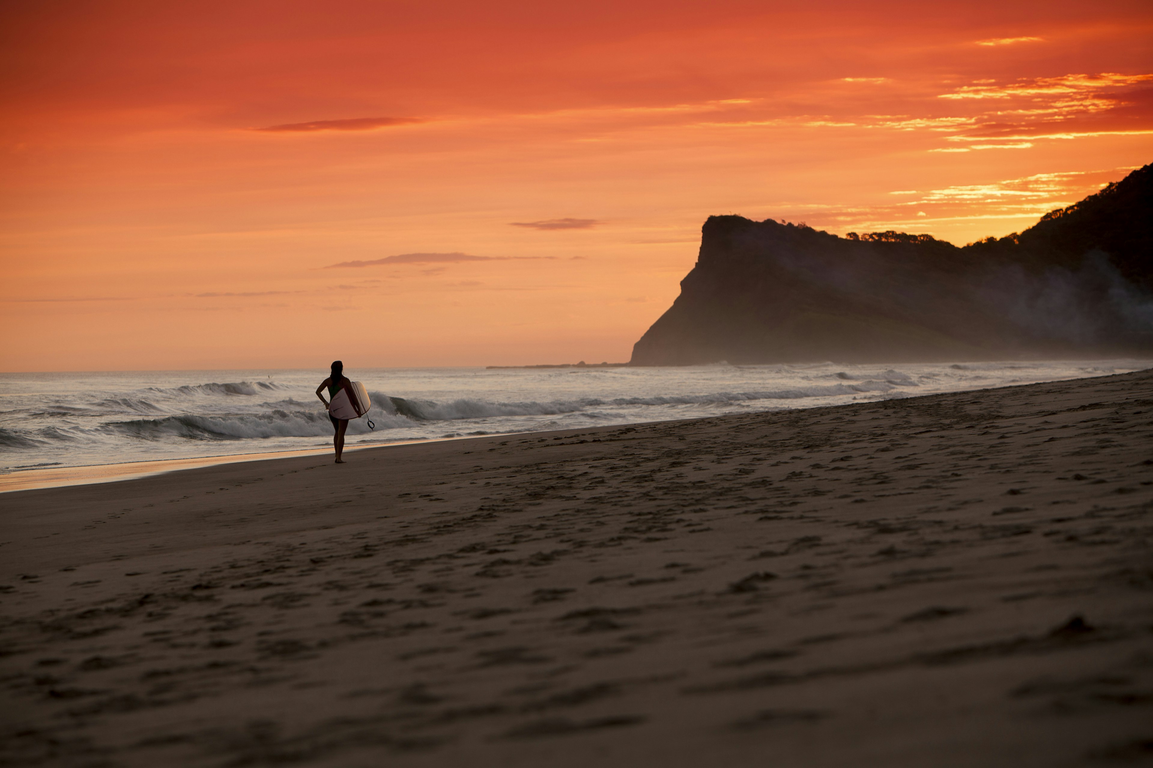 A silhouetted surfer walks down a beach in Nicaragua on sunset during a balmy June afternoon.