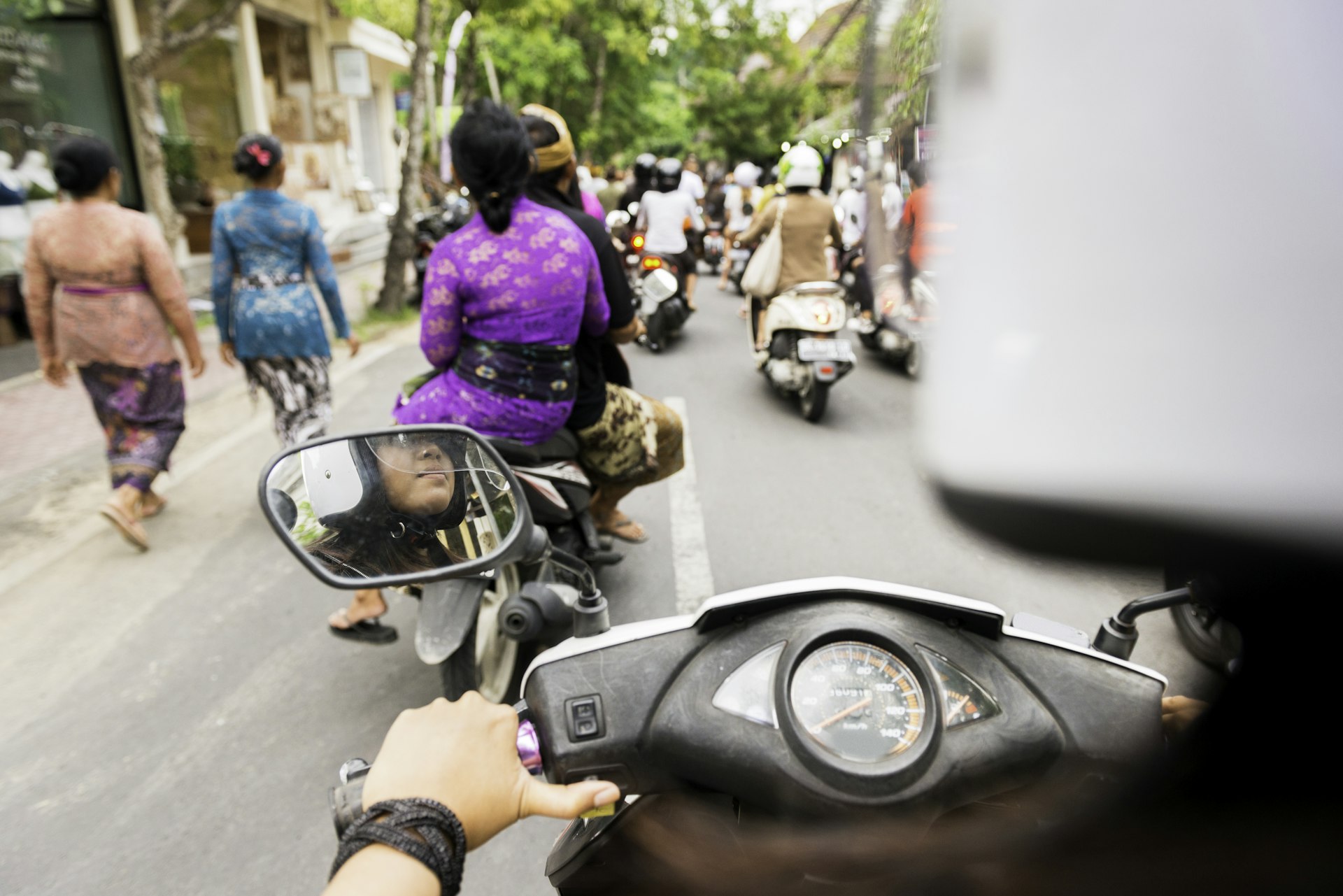 A line of motorcycle riders heading down a narrow street in an urban area