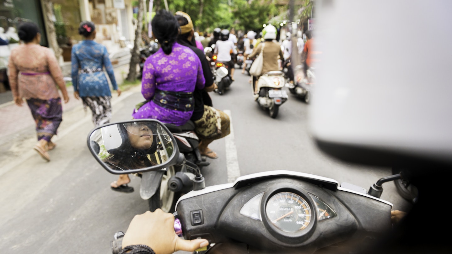 This over the shoulder royalty free, stock photograph is from a motorbike rear passenger point of view. An 18 year old Indonesian woman is driving the vehicle. Her helmet is out of focus in the foreground providing copy space. The road ahead in Ubud, Bali is full of other motor scooters and pedestrians wearing colorful, traditional Balinese clothing during late afternoon rush hour. Photographed with a Nikon D800 DSLR camera.
469663856
Balinese Culture, Real People, Sports Helmet, Over The Shoulder View, Photography, Moped, Personal Perspective, City Life, East Asian Culture, Ubud, Rush Hour, Motor Scooter, Color Image, 18-19 Years, Driving, Traffic, Asian Ethnicity, Asian and Indian Ethnicities, Routine, Cultures, Crowded, Full, Travel Destinations, Transportation, Lifestyles, Urban Scene, Outdoors, Horizontal, Bali, Indonesia, Asia, Day, Street, Road, City, Motorcycle, Land Vehicle, Mode of Transport, Common