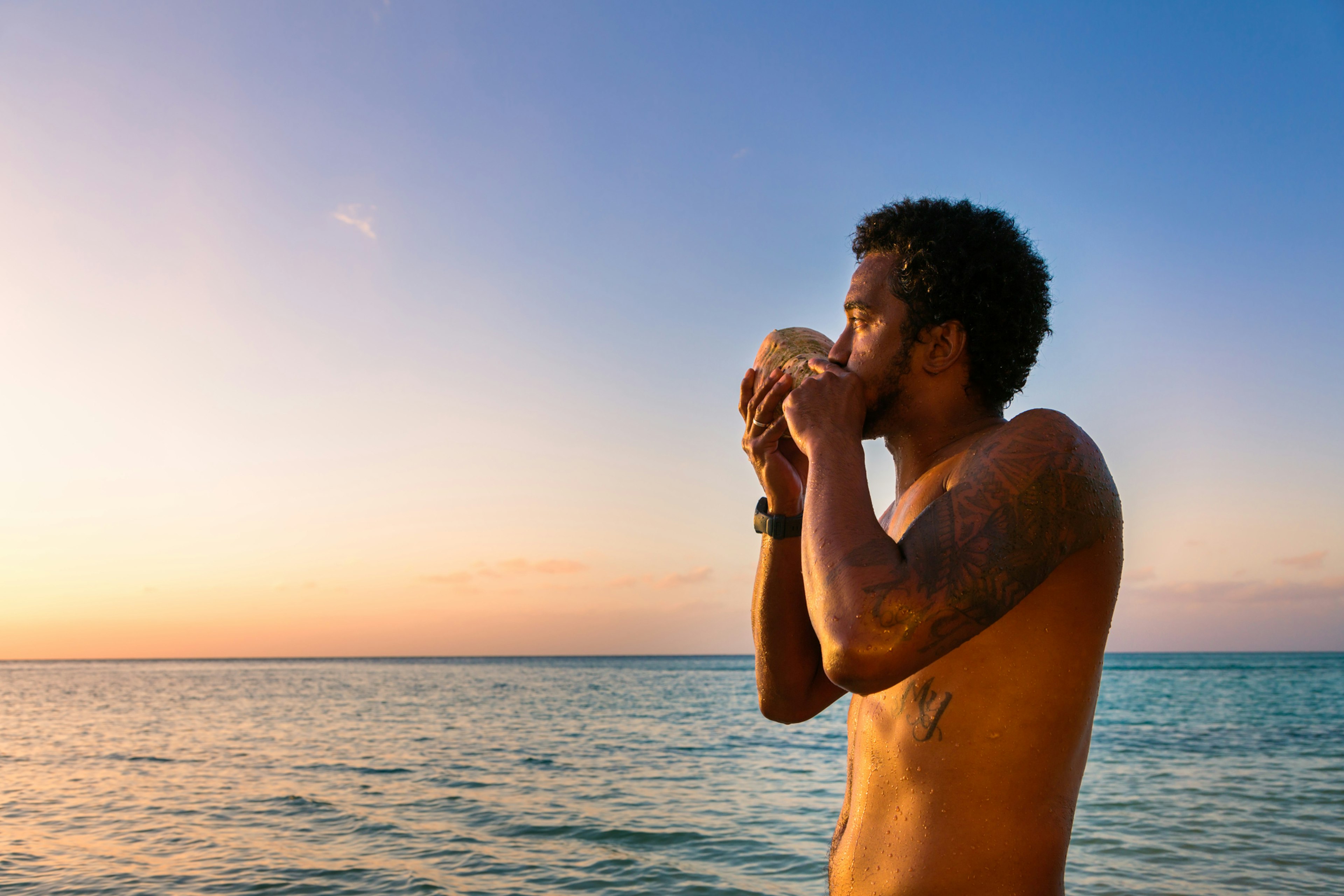 A man blows a traditional conch shell at sunset, Fiji, South Pacific