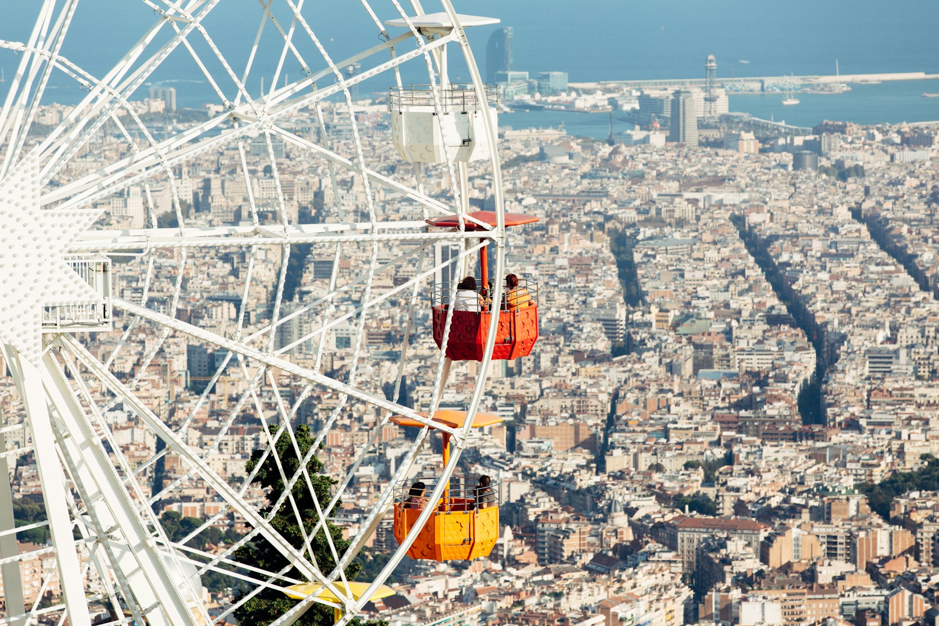 An aerial view of a ferris wheel with brightly colored cars overlooking all of Barcelona