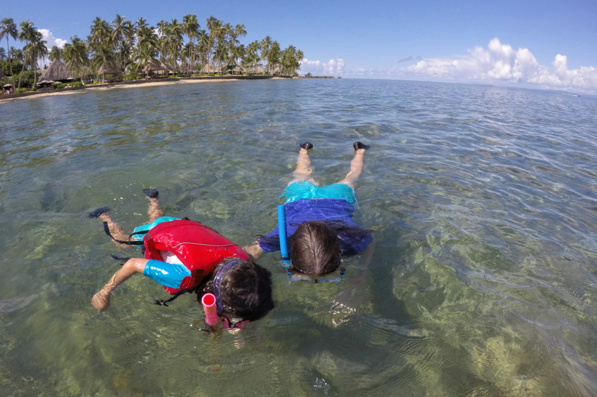 Mother and child snorkel over a coral reef in a tropical resort