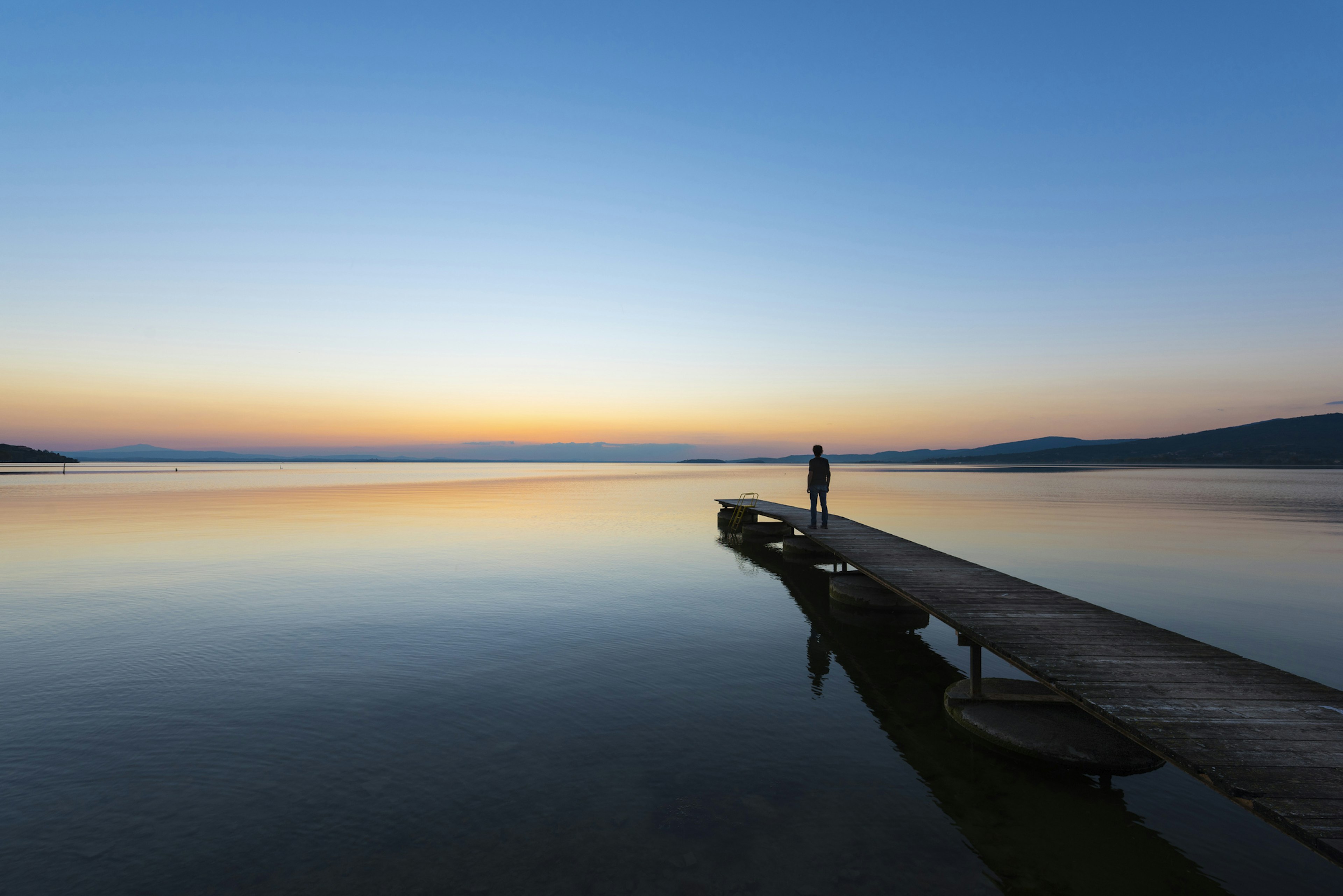 A man stands at the edge of Lake Trasimeno in Italy at sunset