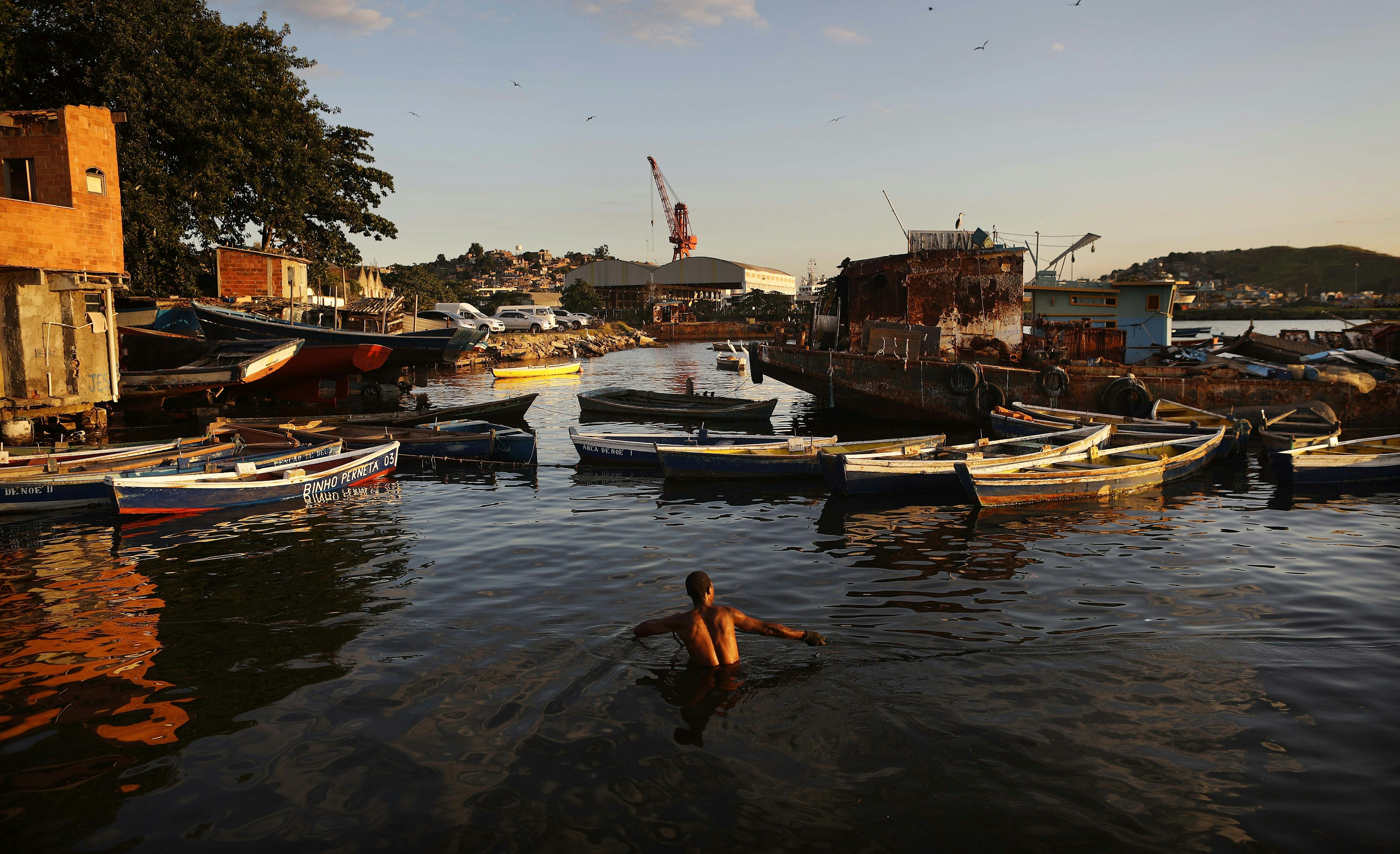 fisherman helps tow a boat to shore along the coast of the polluted Guanabara Bay, Rio de Janeiro, Brazil