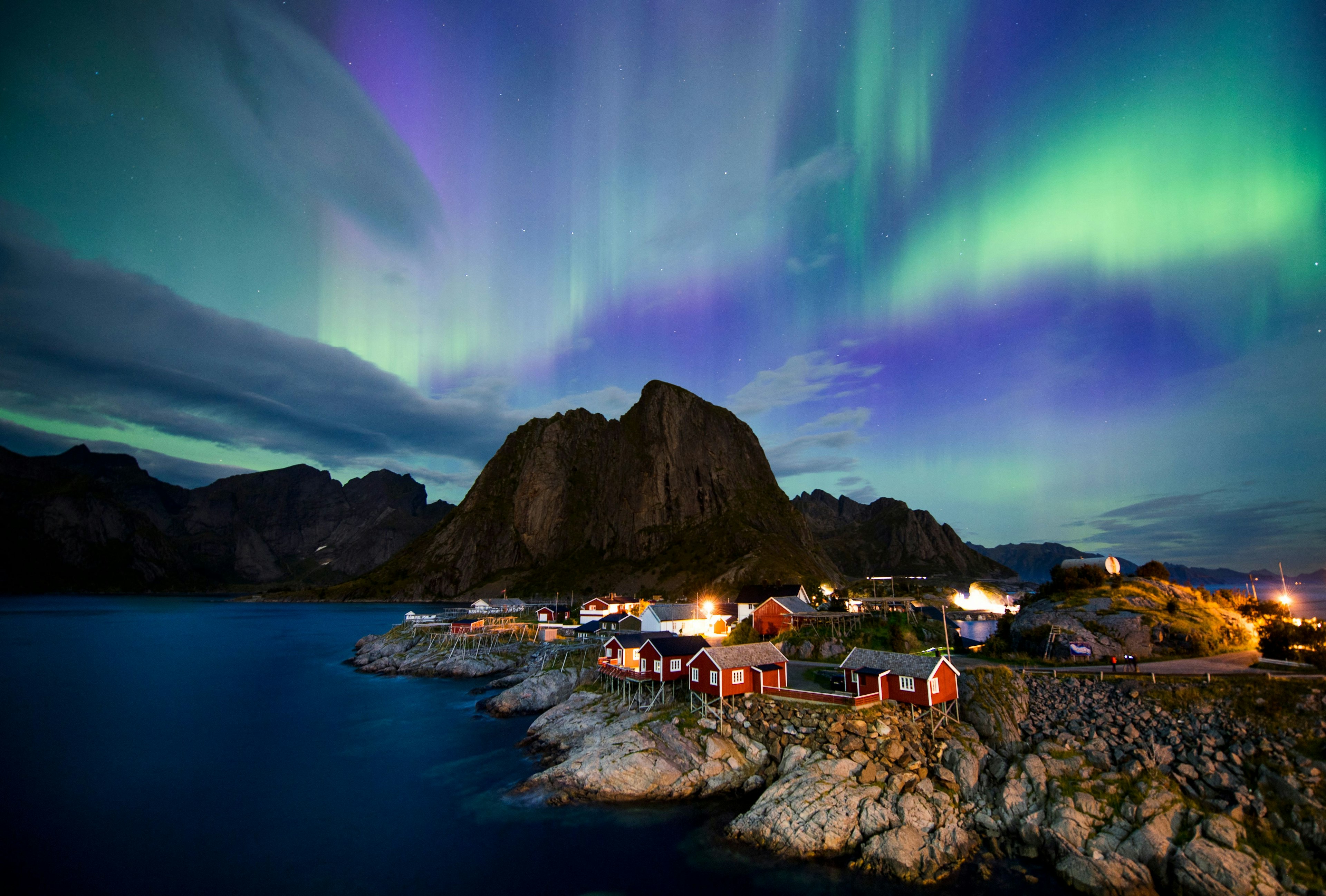 Green, purple and blue streaks of the northern lights fill the night sky over a small island settlement