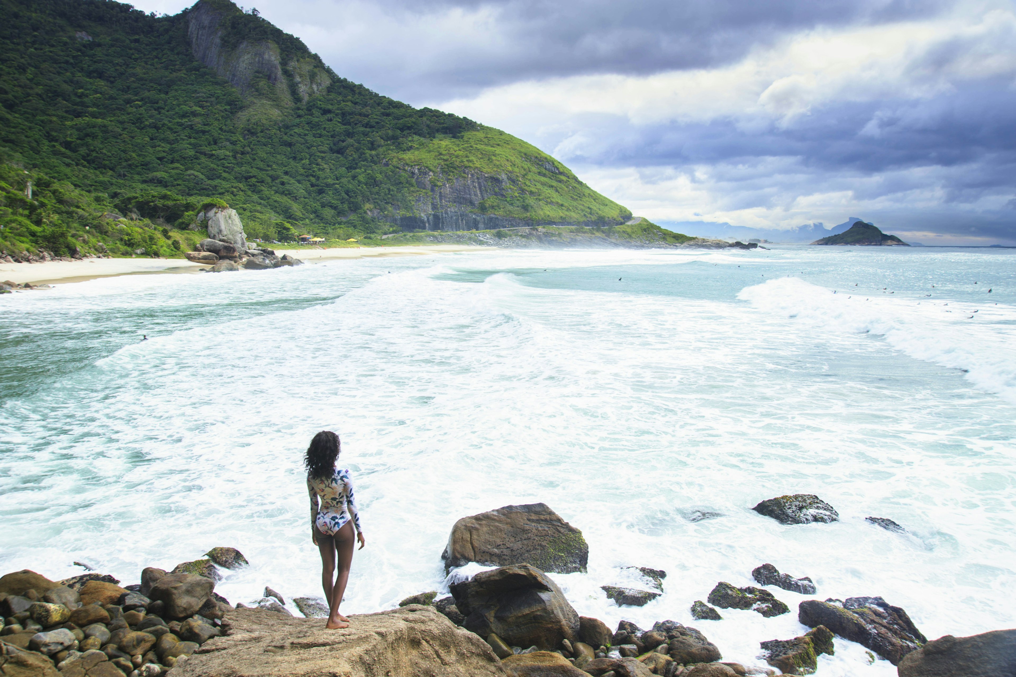 Rear view of a young African-American woman in a one-piece swimsuit looking out over a deserted beach under stormy skies