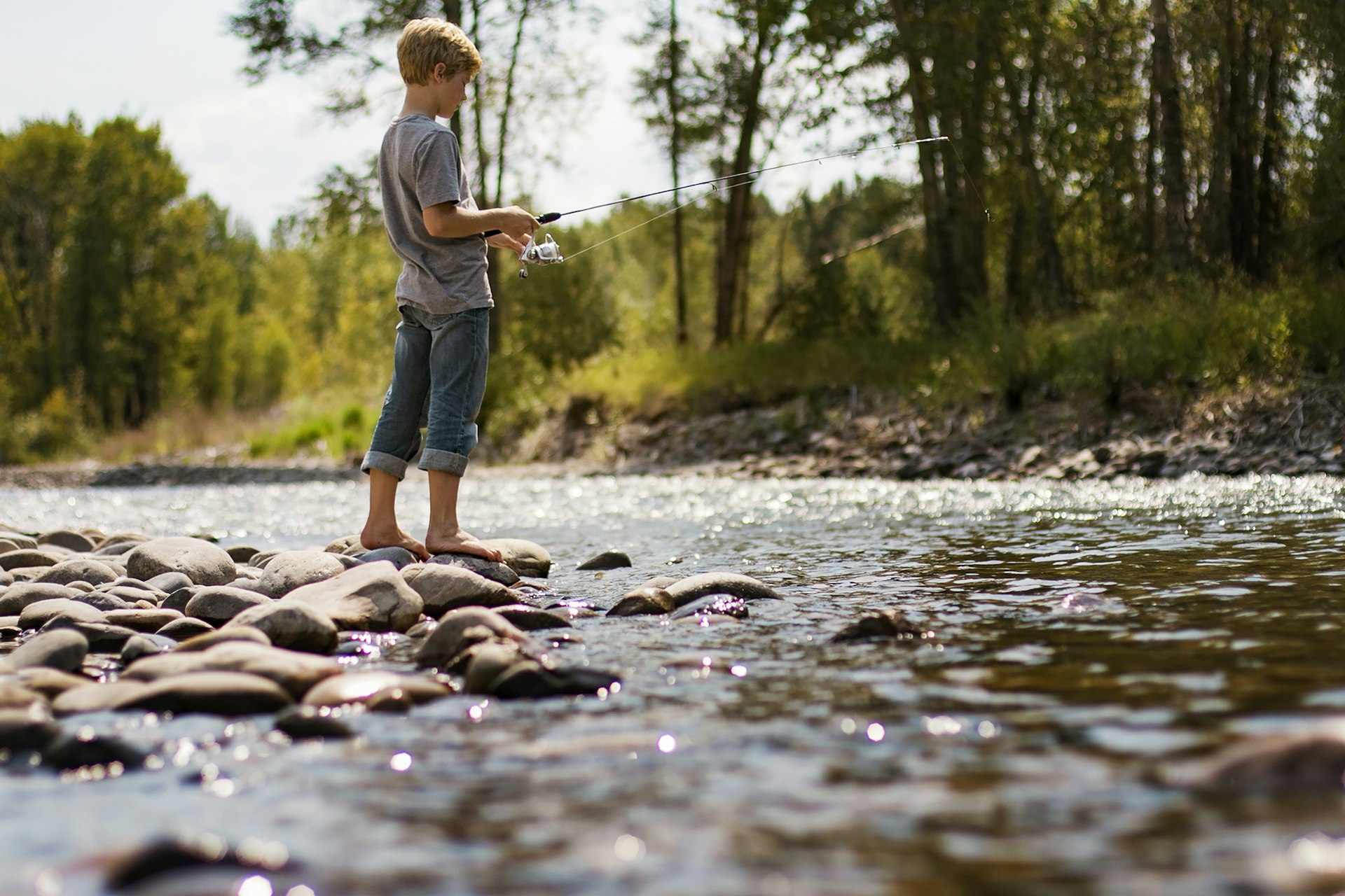 A young boy fishes in a river near Bozeman, Montana in the afternoon sun