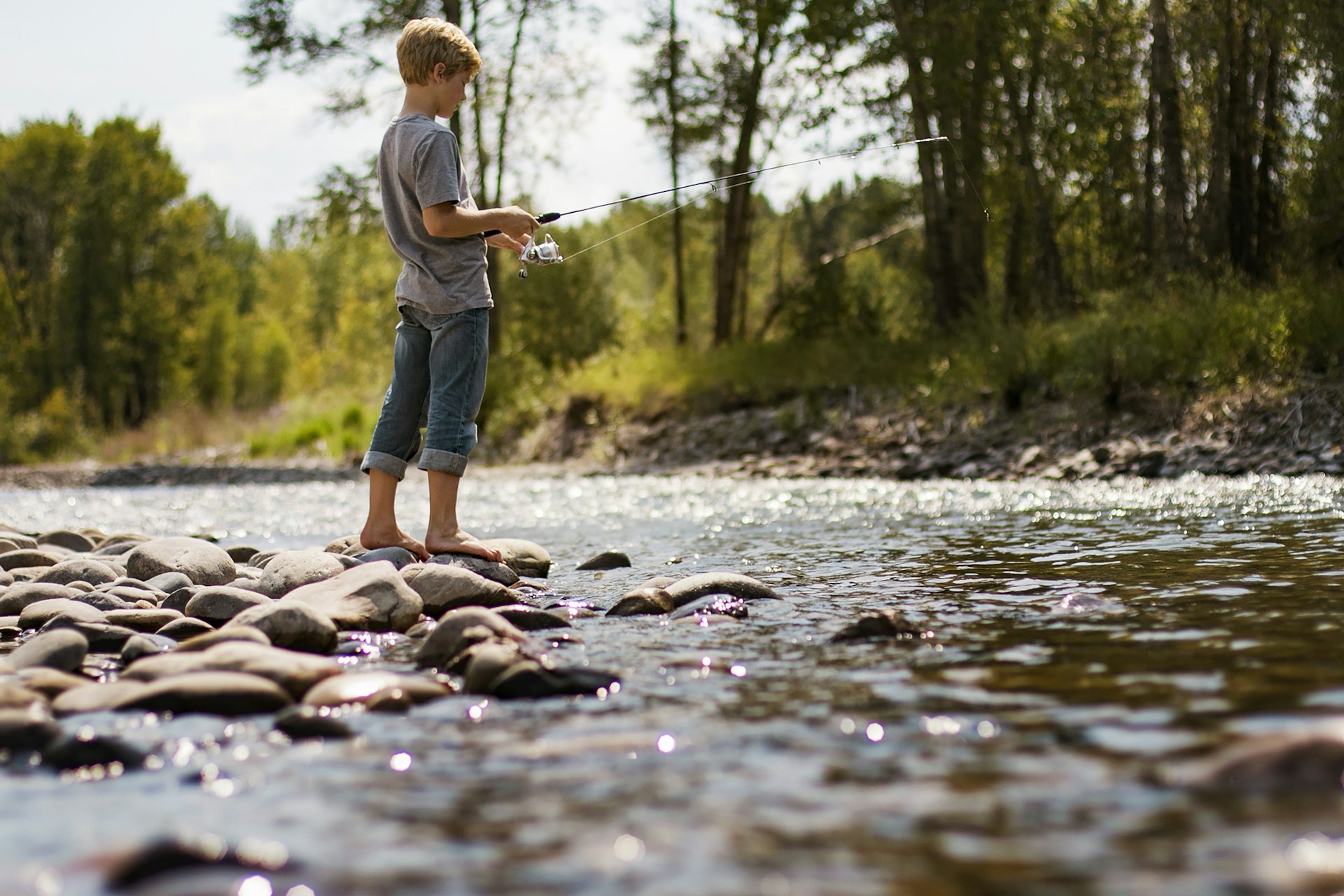 Young Girl Standing In Water At Lake Holding Fishing Pole by Cavan Images