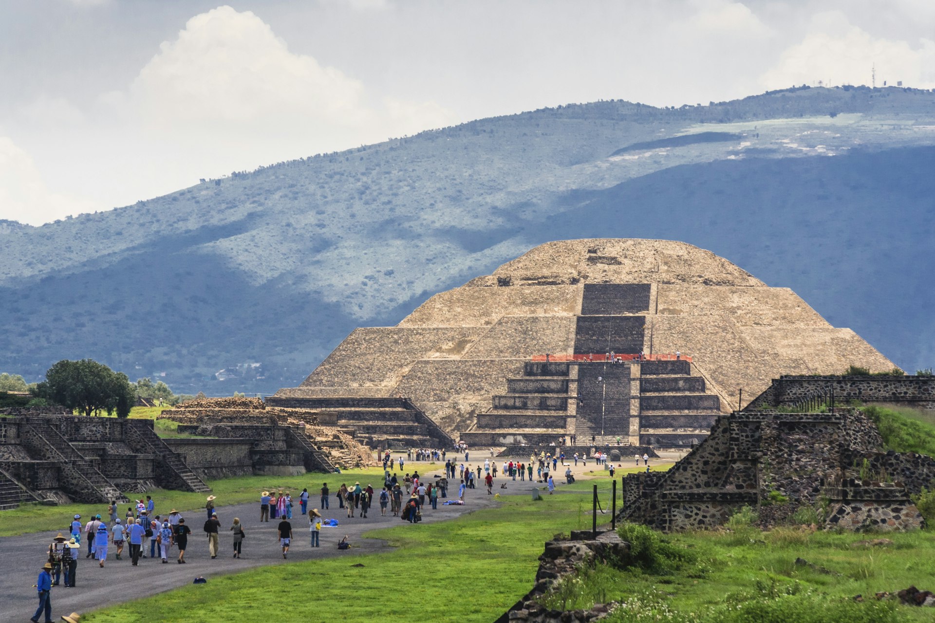 Tourists walk down an avenue leading to a large stone pyramid