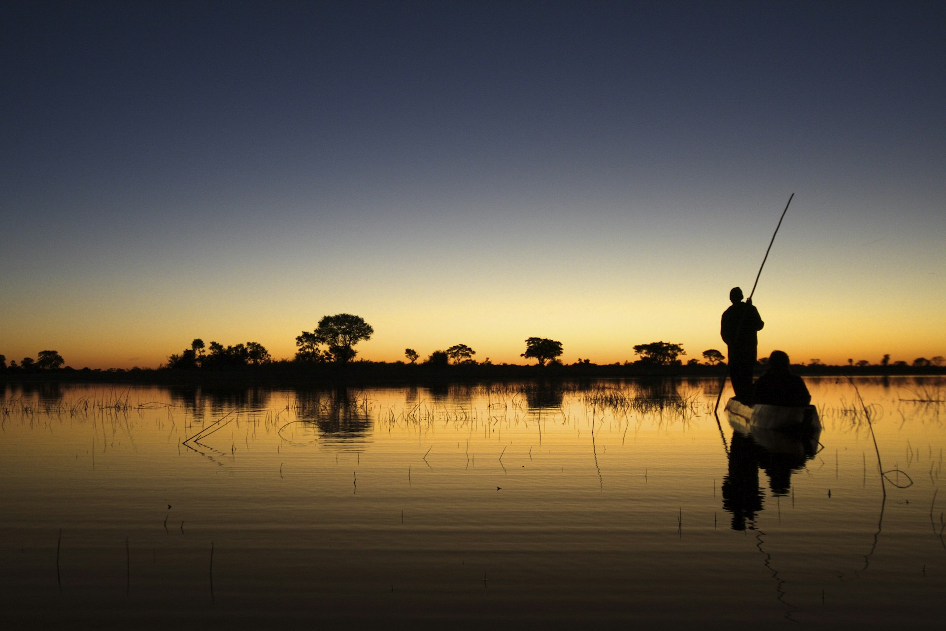 A canoe is silhouetted at dusk floating on Okavango Delta waters in Botswana