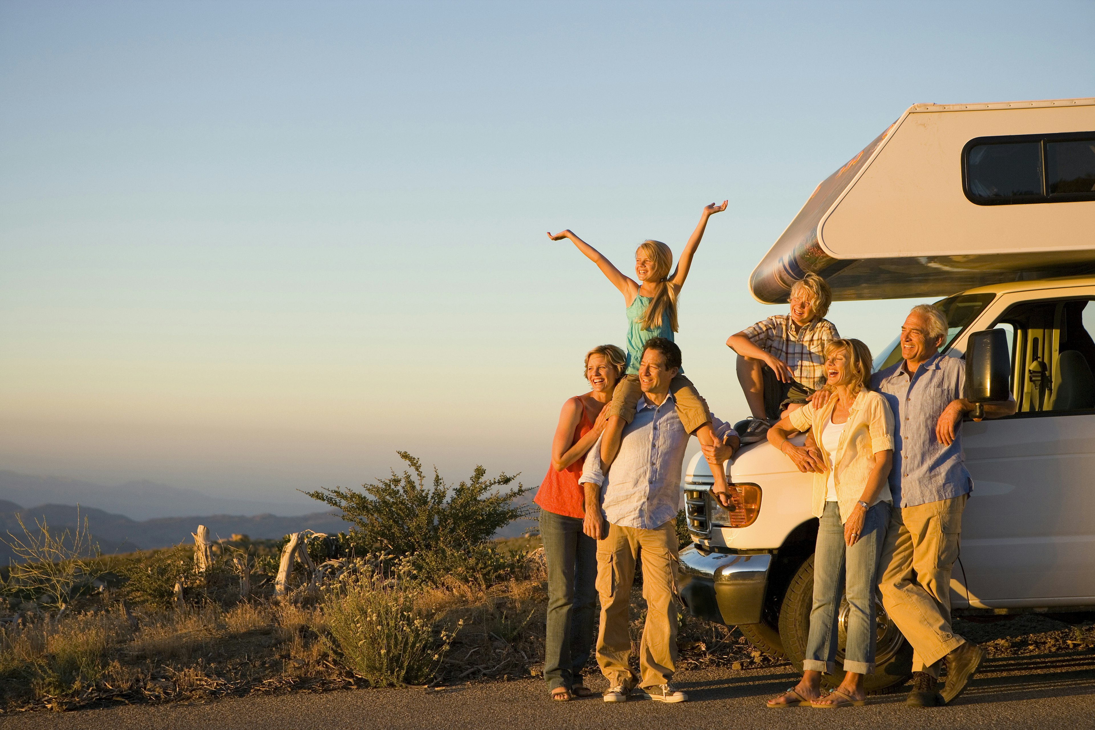 Three generations of a family standing by a motor home on the side of the road at dusk.