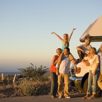 Three generations of a family standing by a motor home on the side of the road at dusk.