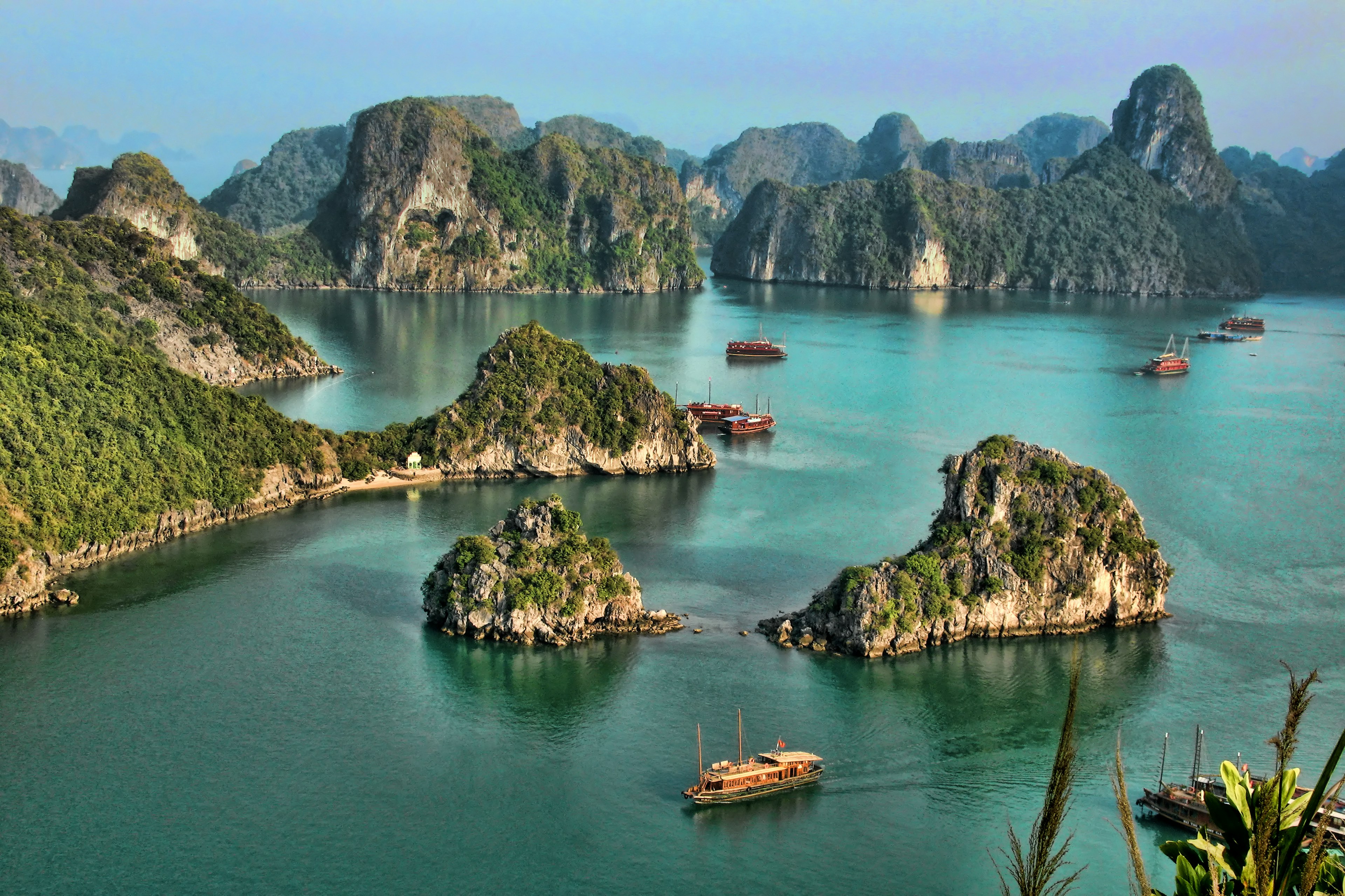 I high vantage point image of a collection of tour boats and cruise ships passing by limestone islands in Halong Bay