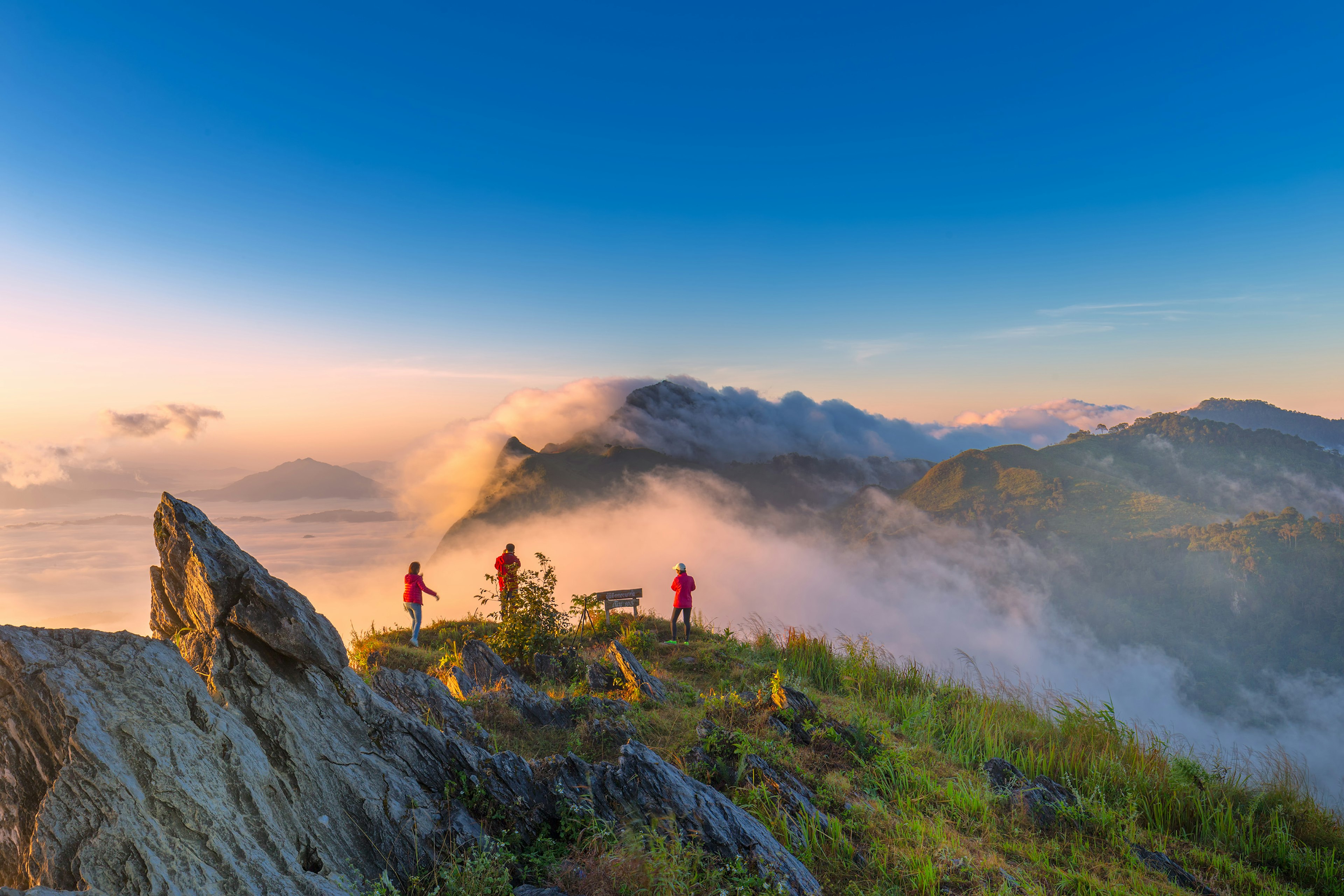 Three people at a viewpoint on top of a mountain as clouds cover some of the surrounding area