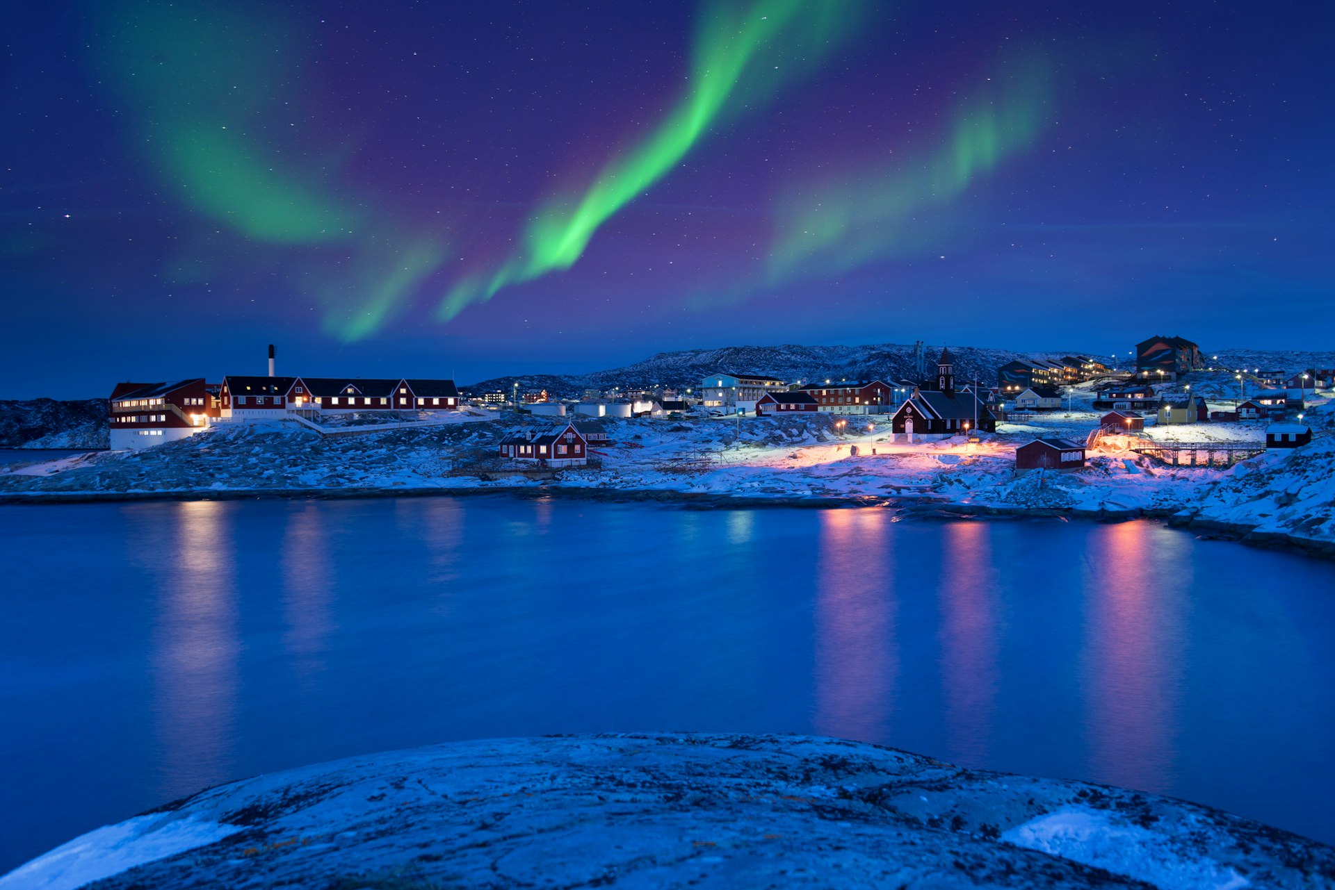 A view across a river to the town of Ilulissat, Greenland showing the Aurora illuminating the sky green