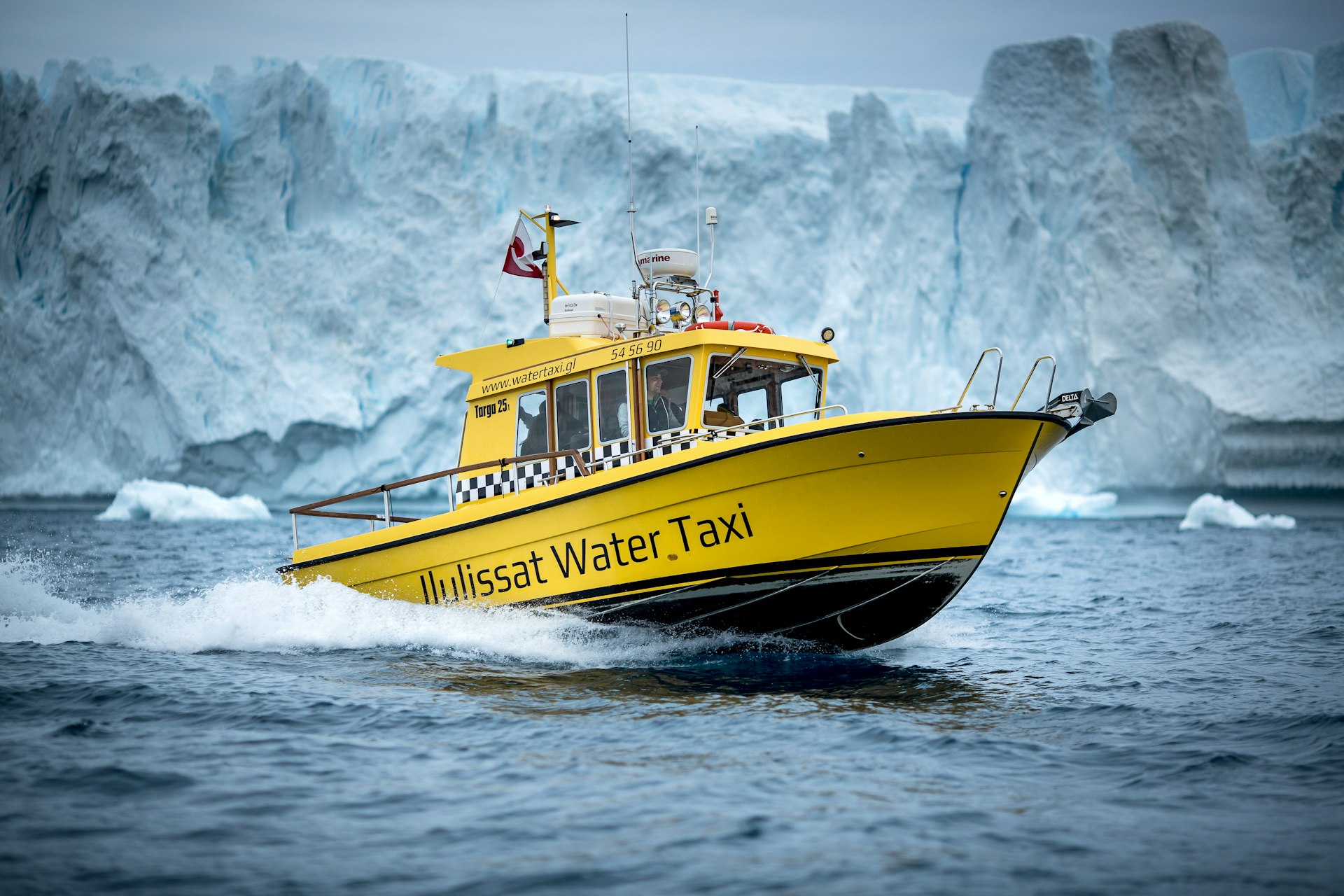 The yellow Ilulissat Water Taxi cuts the water in Greenland in front of icebergs