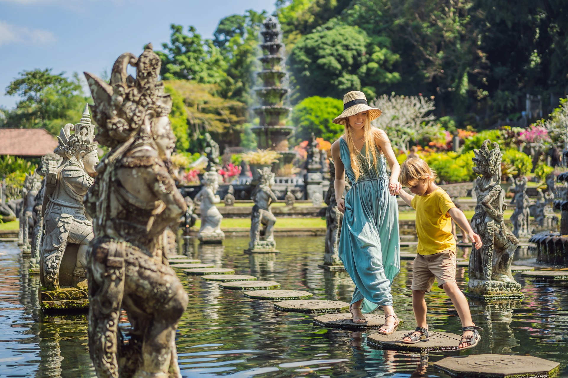 Mom and son tourists walking across stepping stones at Taman Tirta Gangga, Water palace, Water park, Bali Indonesia. 