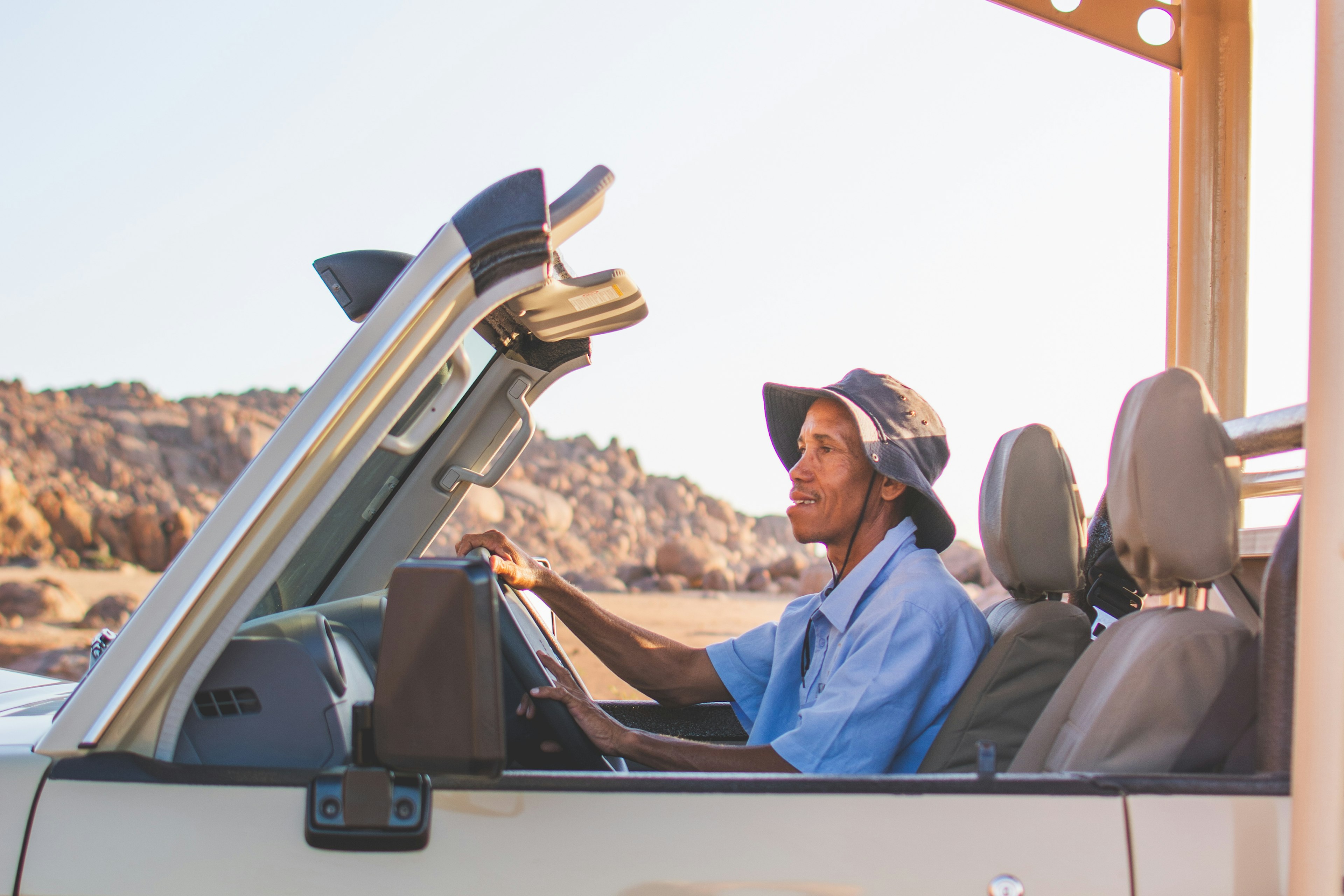 A smiling driver sits in the front of a white car in Namibia