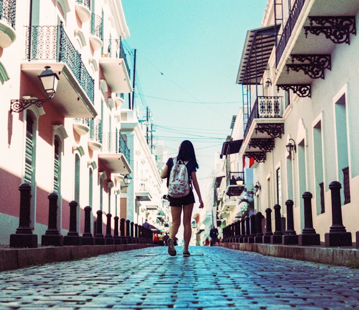 Girl Walking Down Cobblestone Street Surrounded By Colorful Buildings