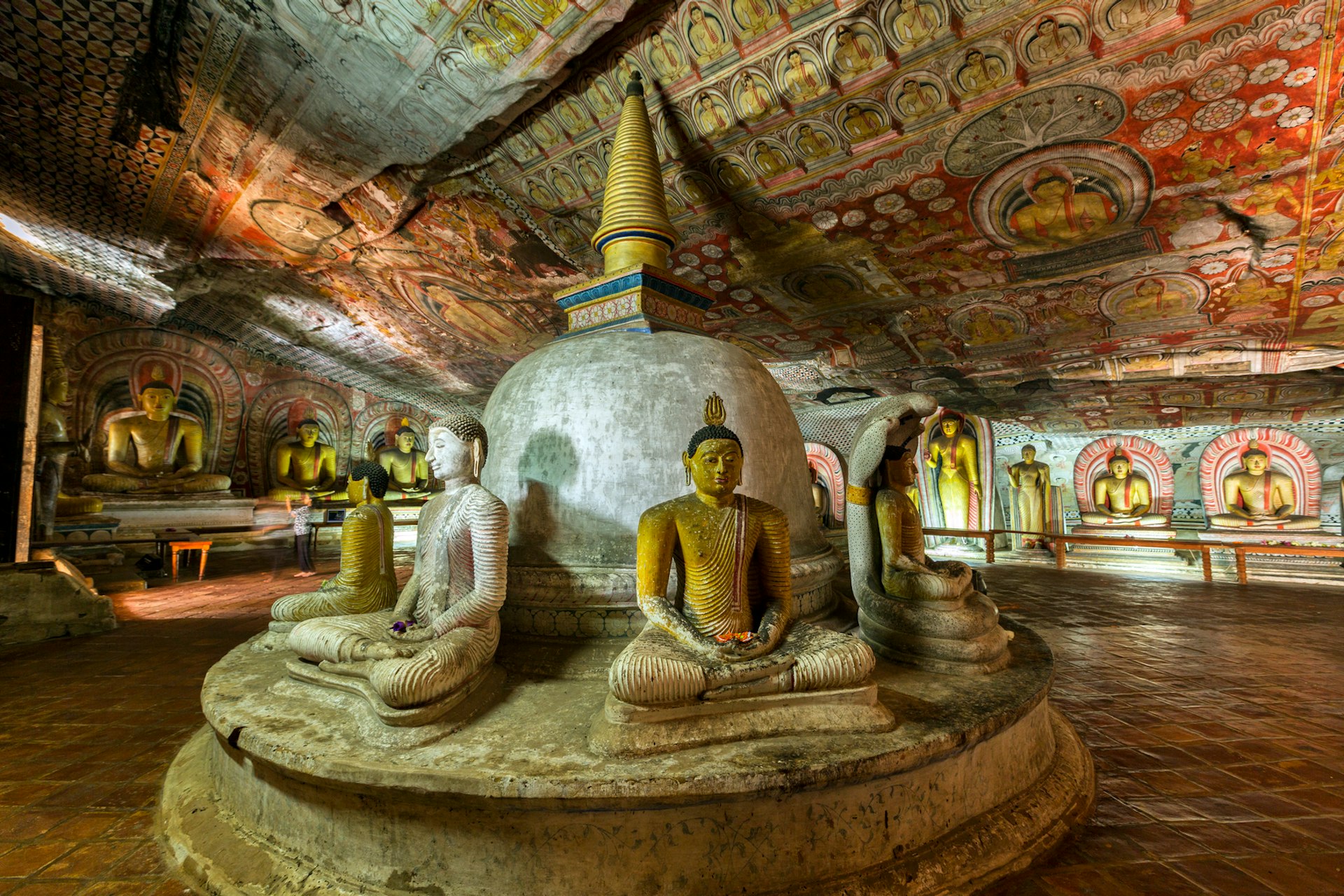 Buddha statues and colorful religious art in the dimly lit caves at Dambulla