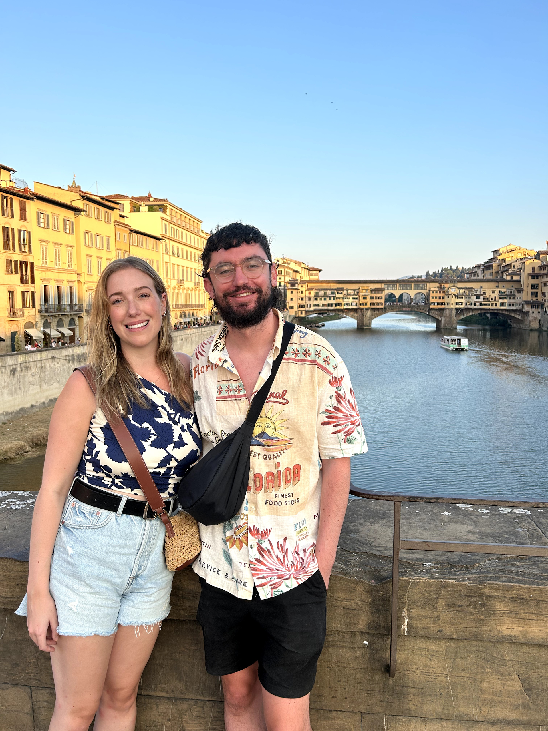 Article author Conall and his partner Amy stand and smile on a bridge in Florence with the river and city in the background