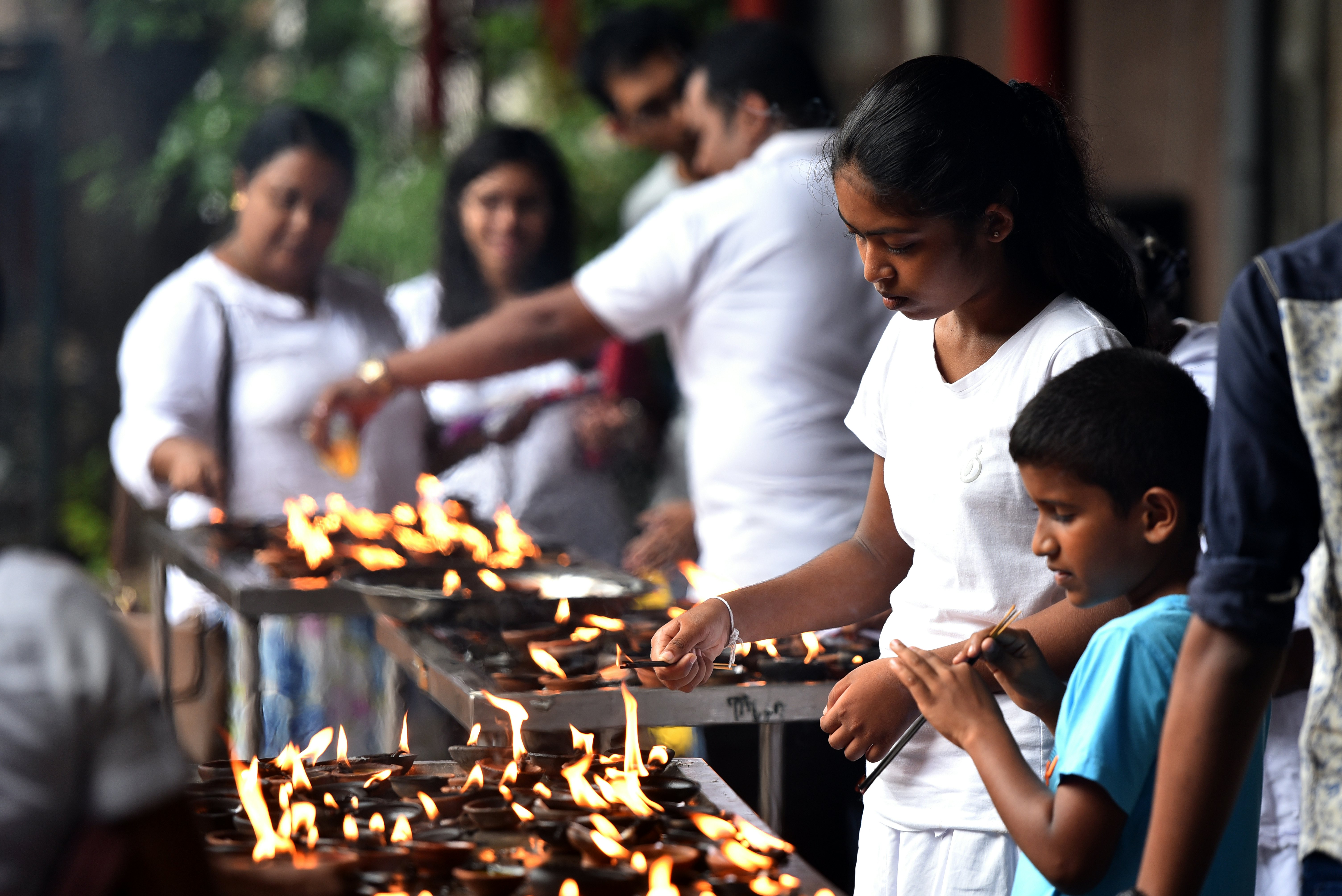 Sri Lankan Buddhists gather at a temple building in front of burning insence